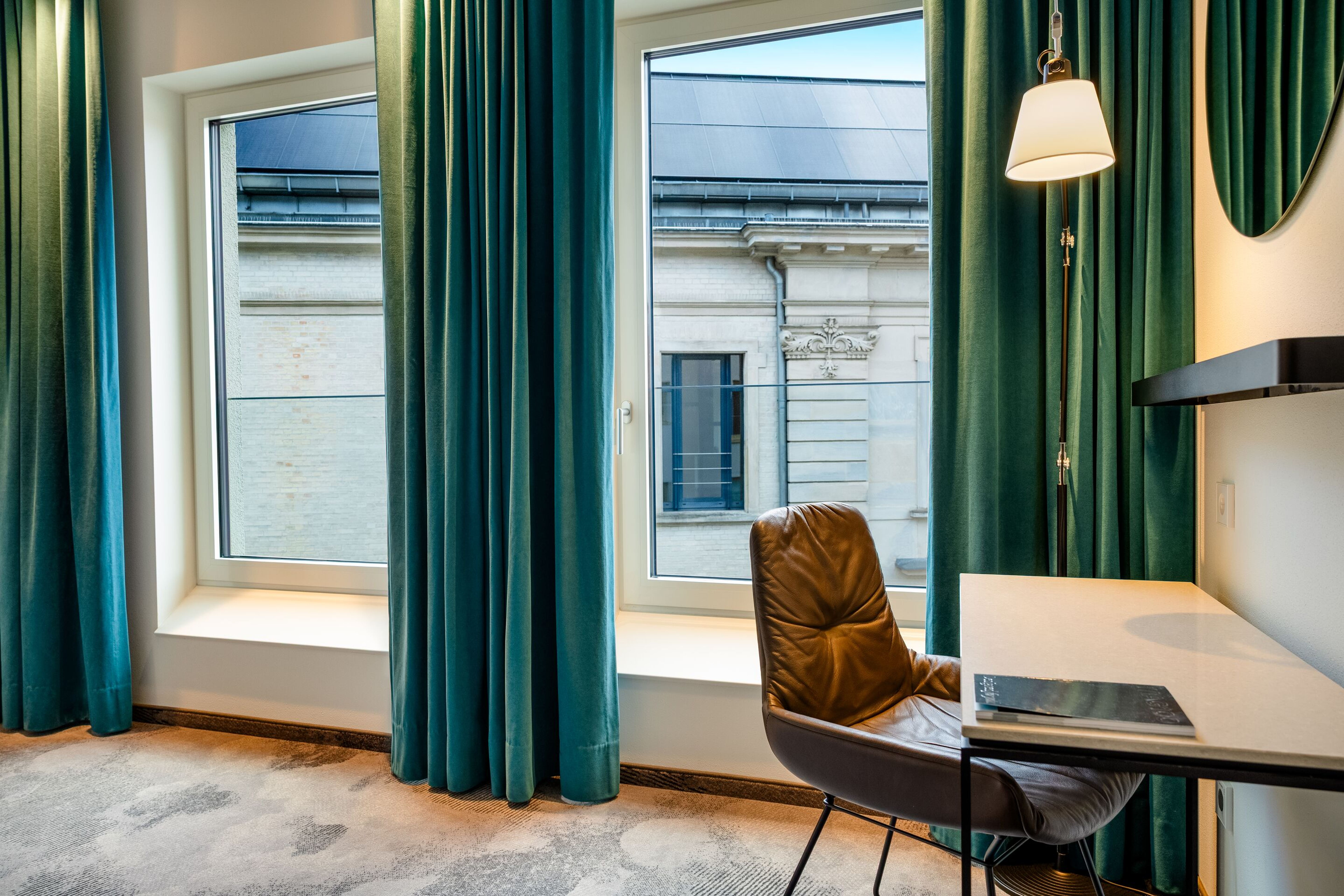 Hotel Motel One Würzburg Helles Hotelzimmer mit großen Fenstern, dunkelgrünen Vorhängen, einem Schreibtisch mit Stuhl und einer Wandlampe, das eine ruhige Arbeitsatmosphäre bietet. Blick auf ein klassisches Gebäude von außen. Hotel Motel One Würzburg Helles Hotelzimmer mit großen Fenstern, dunkelgrünen Vorhängen, einem Schreibtisch mit Stuhl und einer Wandlampe, das eine ruhige Arbeitsatmosphäre bietet. Blick auf ein klassisches Gebäude von außen.