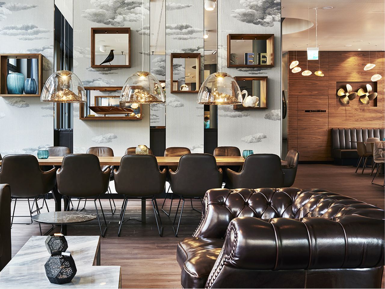 Moderner, stilvoll eingerichteter Essbereich mit langem Holztisch, bequemen Lederstühlen und eleganten Hängeleuchten. Warme Holzakzente und verspiegelte Wände schaffen eine gemütliche Atmosphäre zum Verweilen.