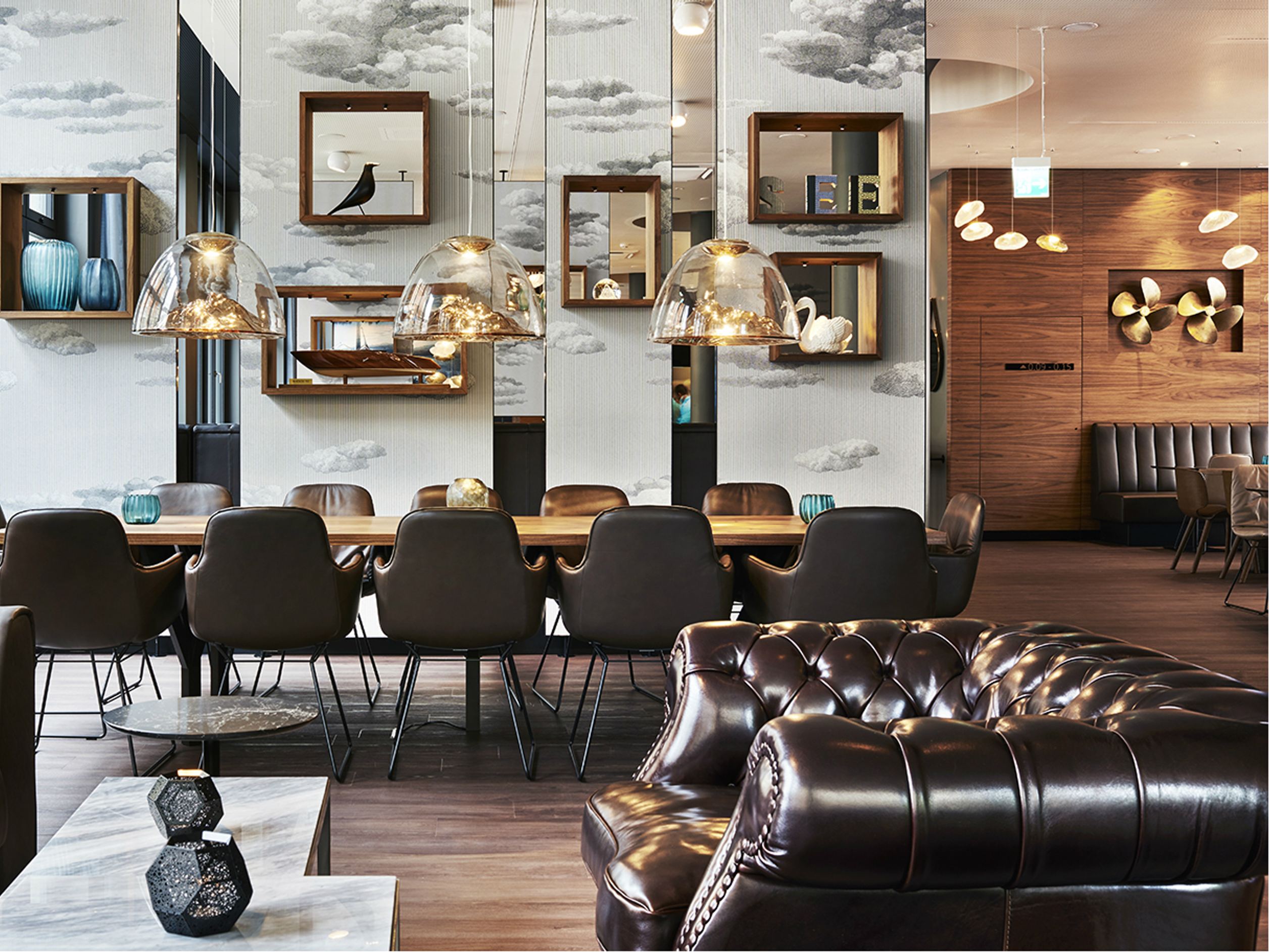 Moderner, stilvoll eingerichteter Essbereich mit langem Holztisch, bequemen Lederstühlen und eleganten Hängeleuchten. Warme Holzakzente und verspiegelte Wände schaffen eine gemütliche Atmosphäre zum Verweilen.