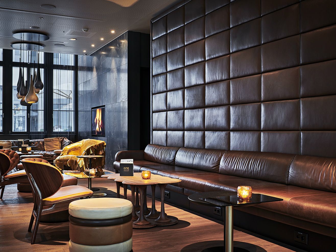 Elegante Hotel-Lounge mit braunem Leder-Sitzbereich, warmem Kaminfeuer und sanfter Beleuchtung für entspannte Atmosphäre und gemütlichen Aufenthalt.