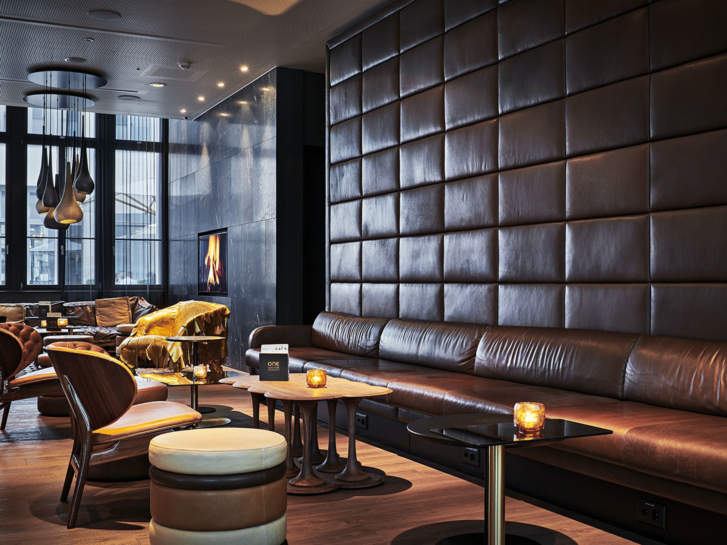 Elegante Hotel-Lounge mit braunem Leder-Sitzbereich, warmem Kaminfeuer und sanfter Beleuchtung für entspannte Atmosphäre und gemütlichen Aufenthalt.