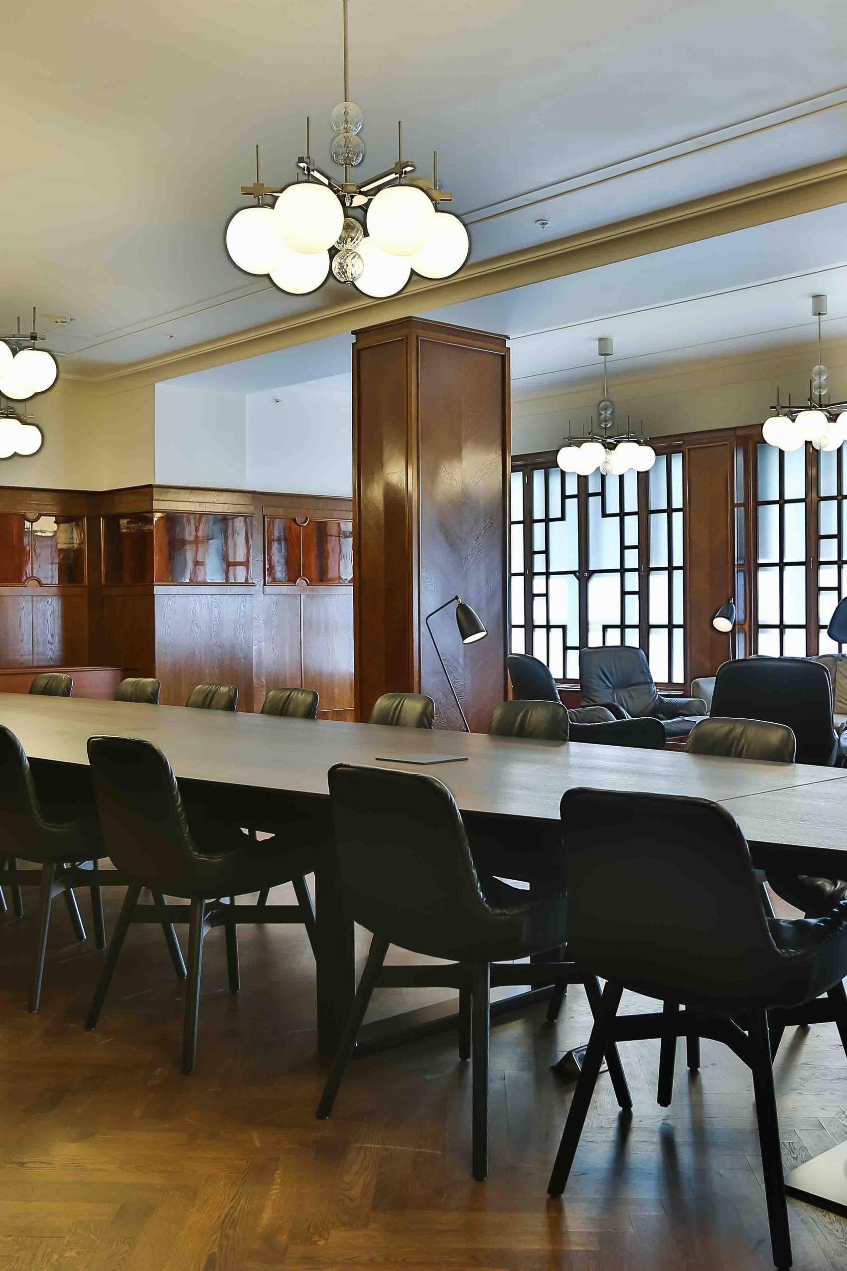 Motel One Prag Florentinum Konferenzraum mit langem Tisch und bequemen Stühlen, warme Holzvertäfelung, große Fenster für viel Tageslicht, moderne Deckenleuchten, ideal für geschäftliche Meetings und Besprechungen in stilvollem Ambiente.