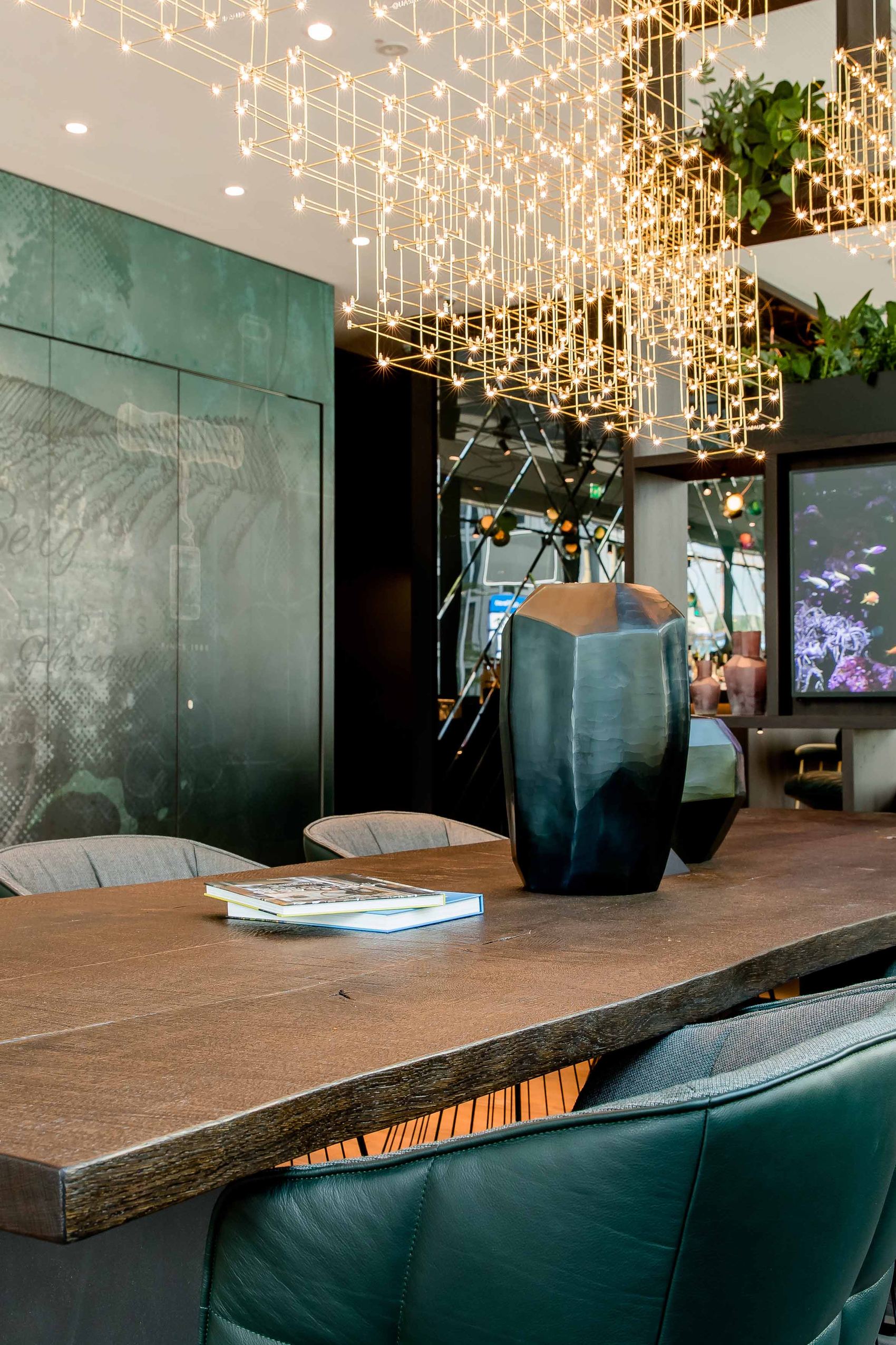 Motel One Konferenzraum mit langem Holztisch, bequemen Lederstühlen, stilvollem Blumendekor und indirekter Beleuchtung, ideal für Meetings oder entspannte Gespräche in einem eleganten Ambiente.