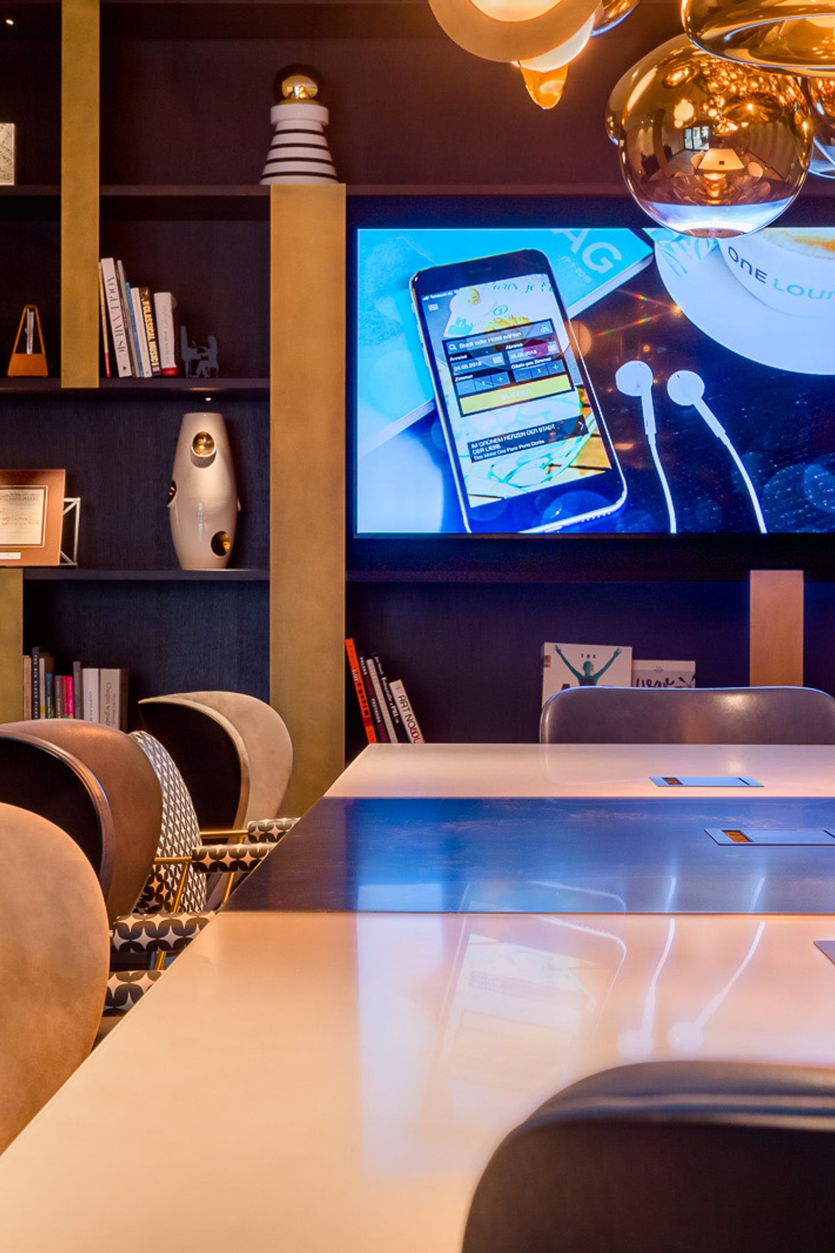 Motel One Besprechungsraum mit ergonomischen Stühlen, beleuchteten Regalen und dekorativen Schriftzügen „CHOPIN“ und „MUSIC“. Ein großer Bildschirm zeigt digitale Inhalte, das Ambiente wirkt kreativ und komfortabel.