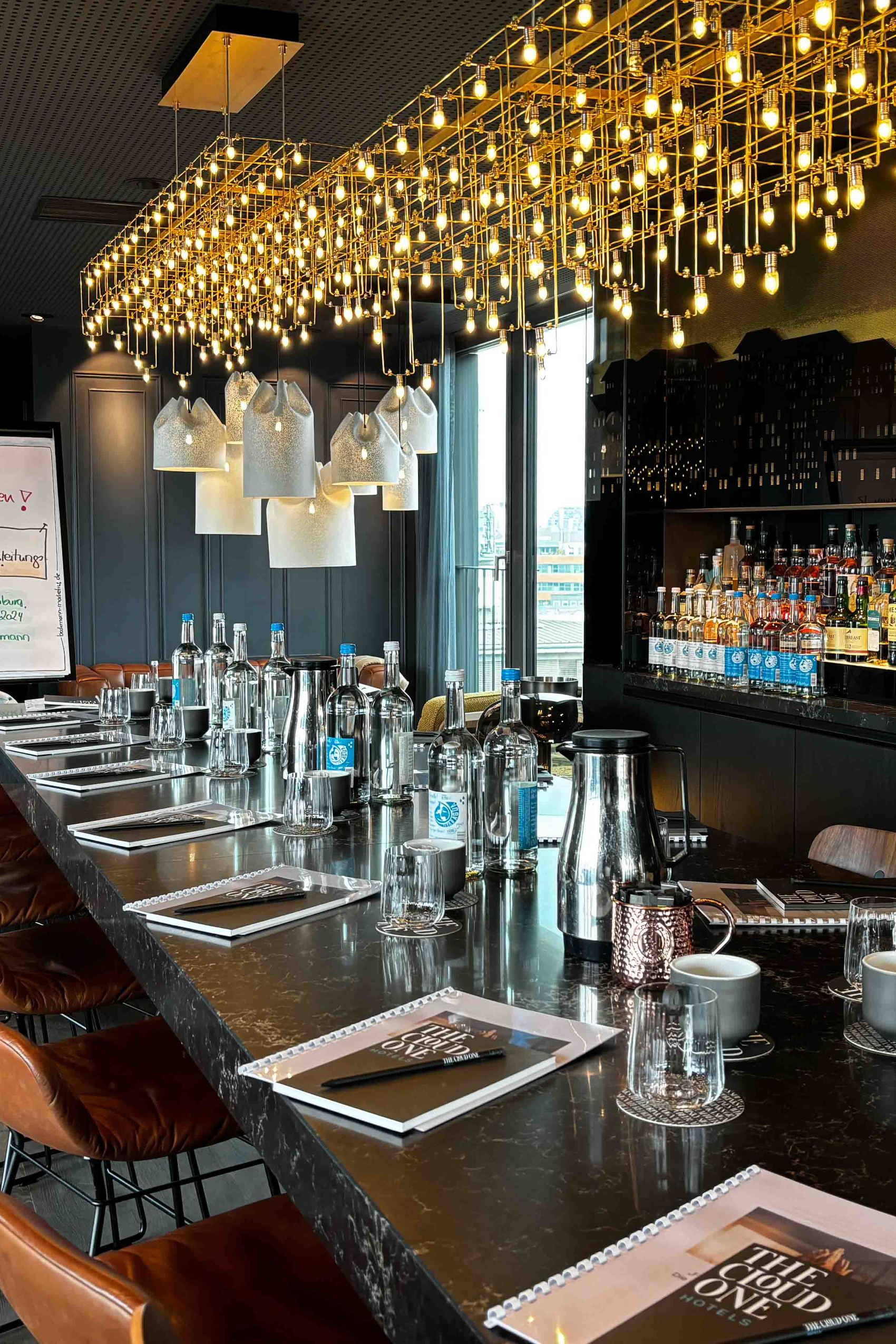 Motel One Hotelbar mit langer Theke, bequemen Lederhockern, stilvoller Beleuchtung und umfangreicher Auswahl an Spirituosen, einladend für gesellige Abende oder entspannte Drinks.