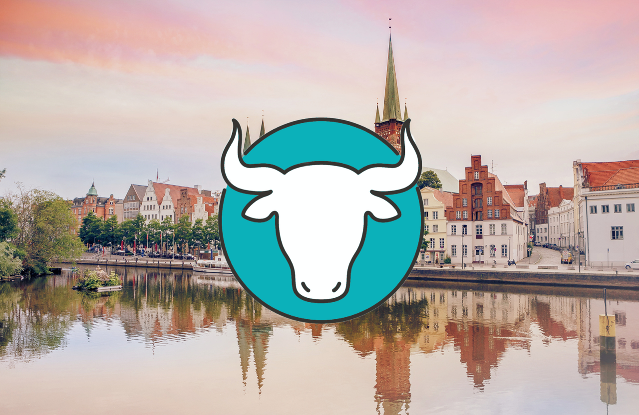 Blick auf die historische Altstadt von Lübeck mit traditionellen Backsteingebäuden am Flussufer, spiegelnd im Wasser, unter einem pastellfarbenen Abendhimmel.