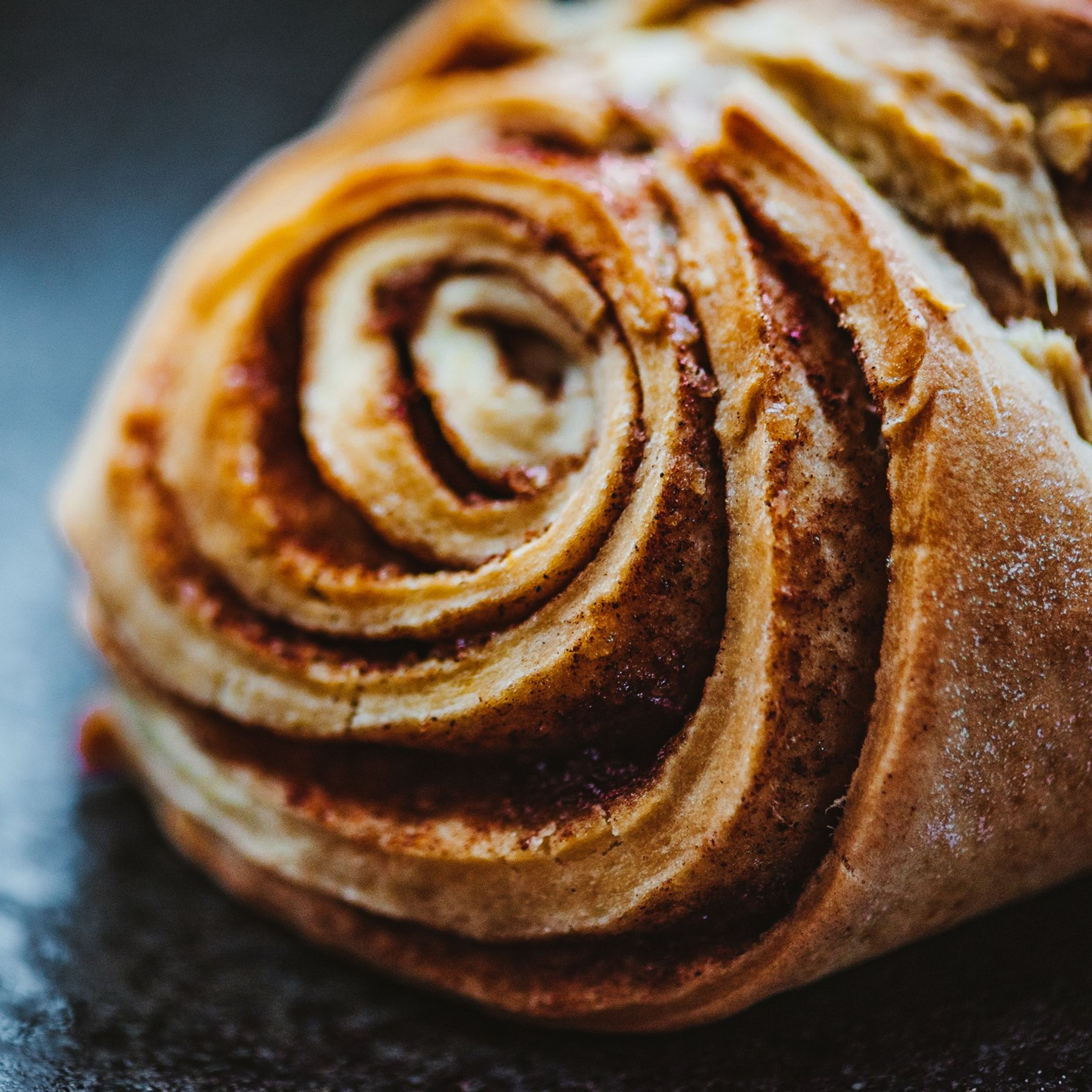 Nahaufnahme einer frisch gebackenen Zimtschnecke mit sichtbaren Zimtspiralen und goldbrauner, knuspriger Kruste.