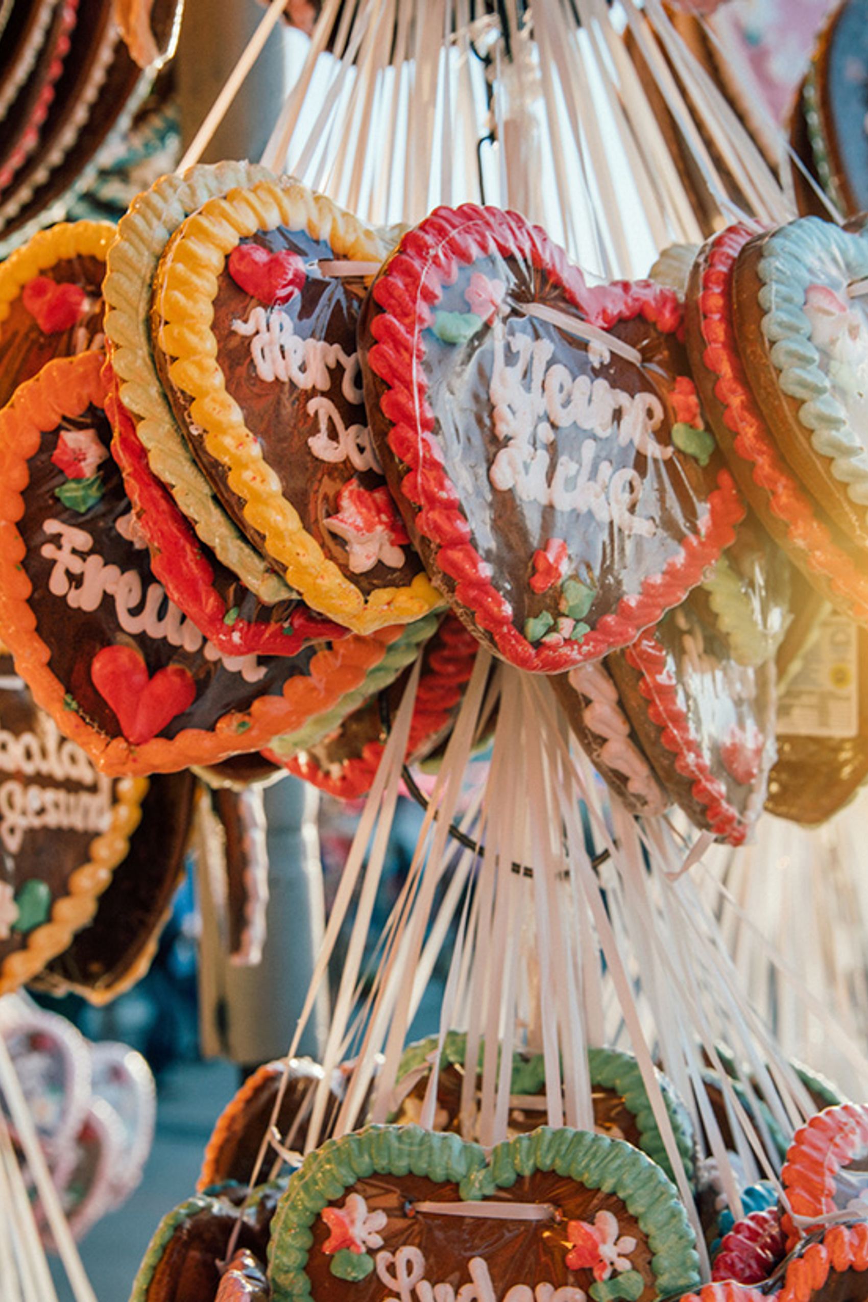 Bunte Lebkuchenherzen mit süßen Verzierungen und kurzen Sprüchen, aufgehängt an Bändern, in warmem Sonnenlicht.
