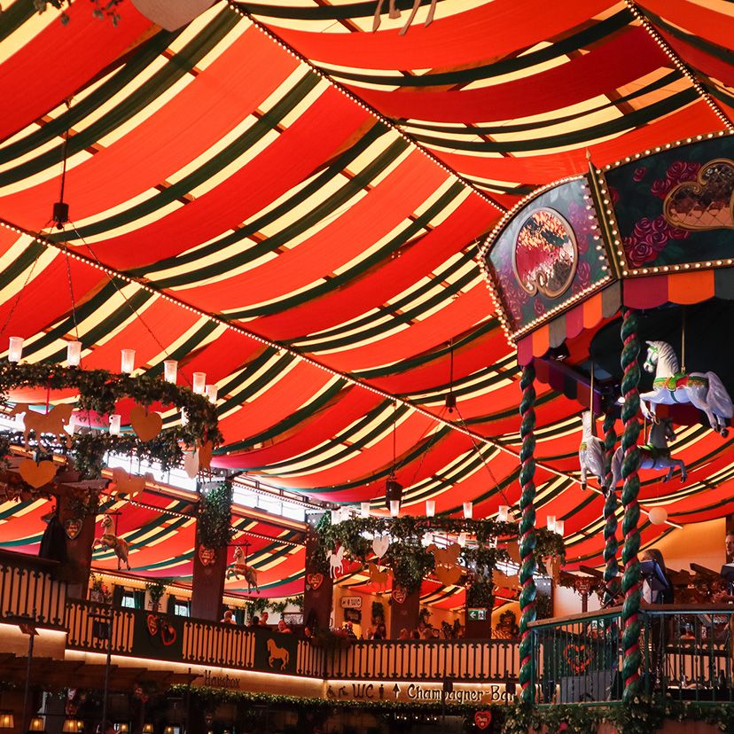 Bunt beleuchtetes Festzelt mit rot-weiß gestreiftem Dach, dekorativem Karussellpferd und festlich geschmückten Kränzen.