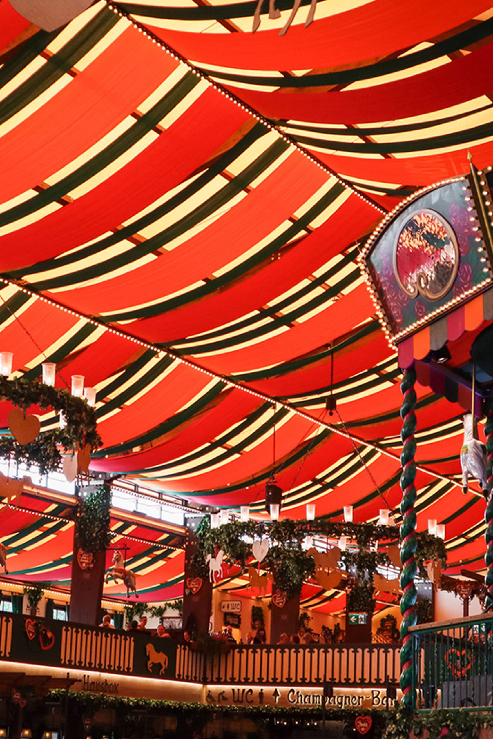 Bunt beleuchtetes Festzelt mit rot-weiß gestreiftem Dach, dekorativem Karussellpferd und festlich geschmückten Kränzen.