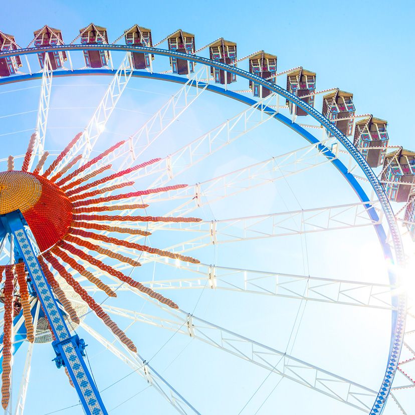 Riesiges Riesenrad mit geschlossenen Gondeln vor hellem, blauem Himmel, Sonnenlicht strahlt seitlich herein.