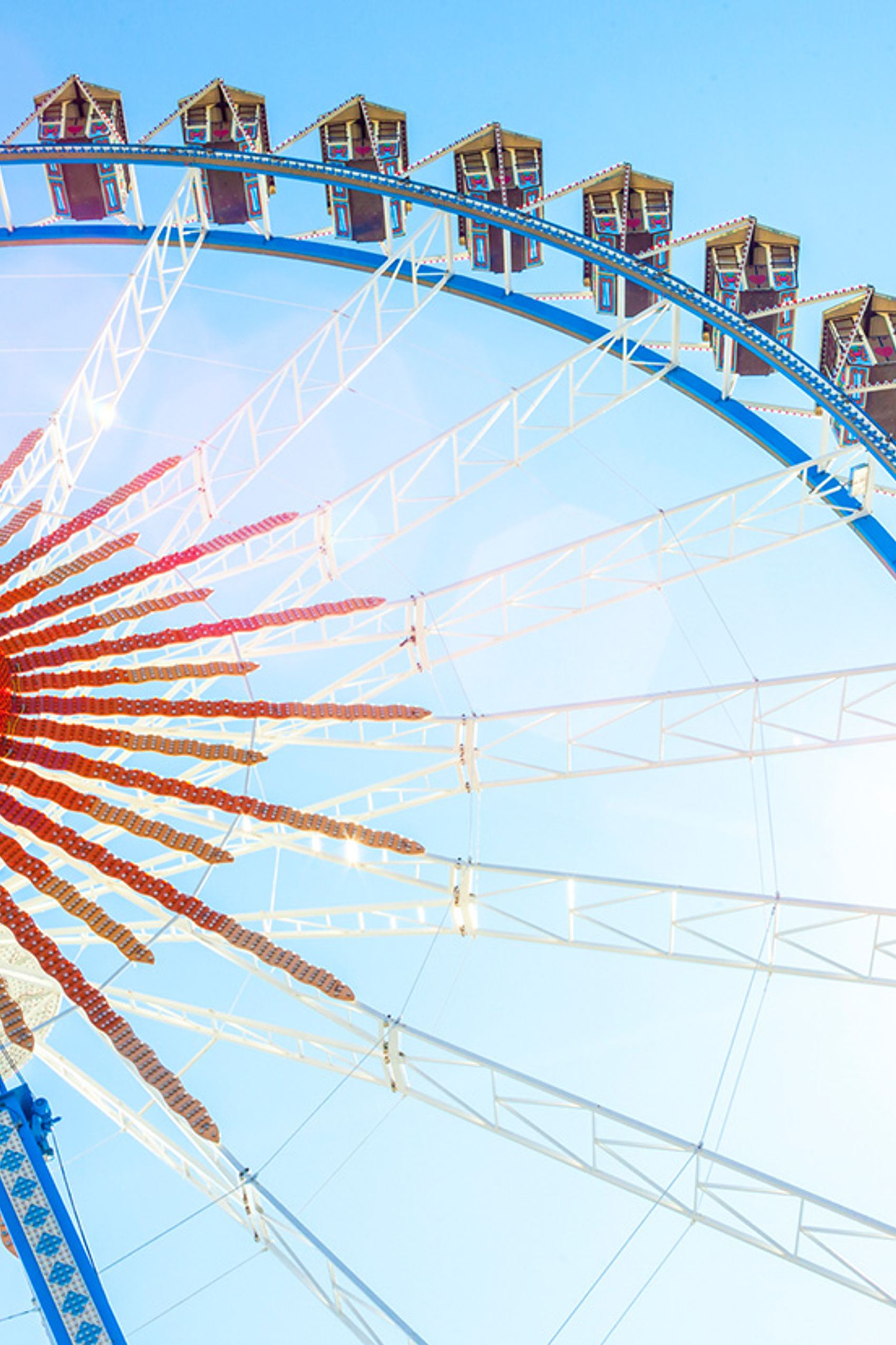 Riesiges Riesenrad mit geschlossenen Gondeln vor hellem, blauem Himmel, Sonnenlicht strahlt seitlich herein.