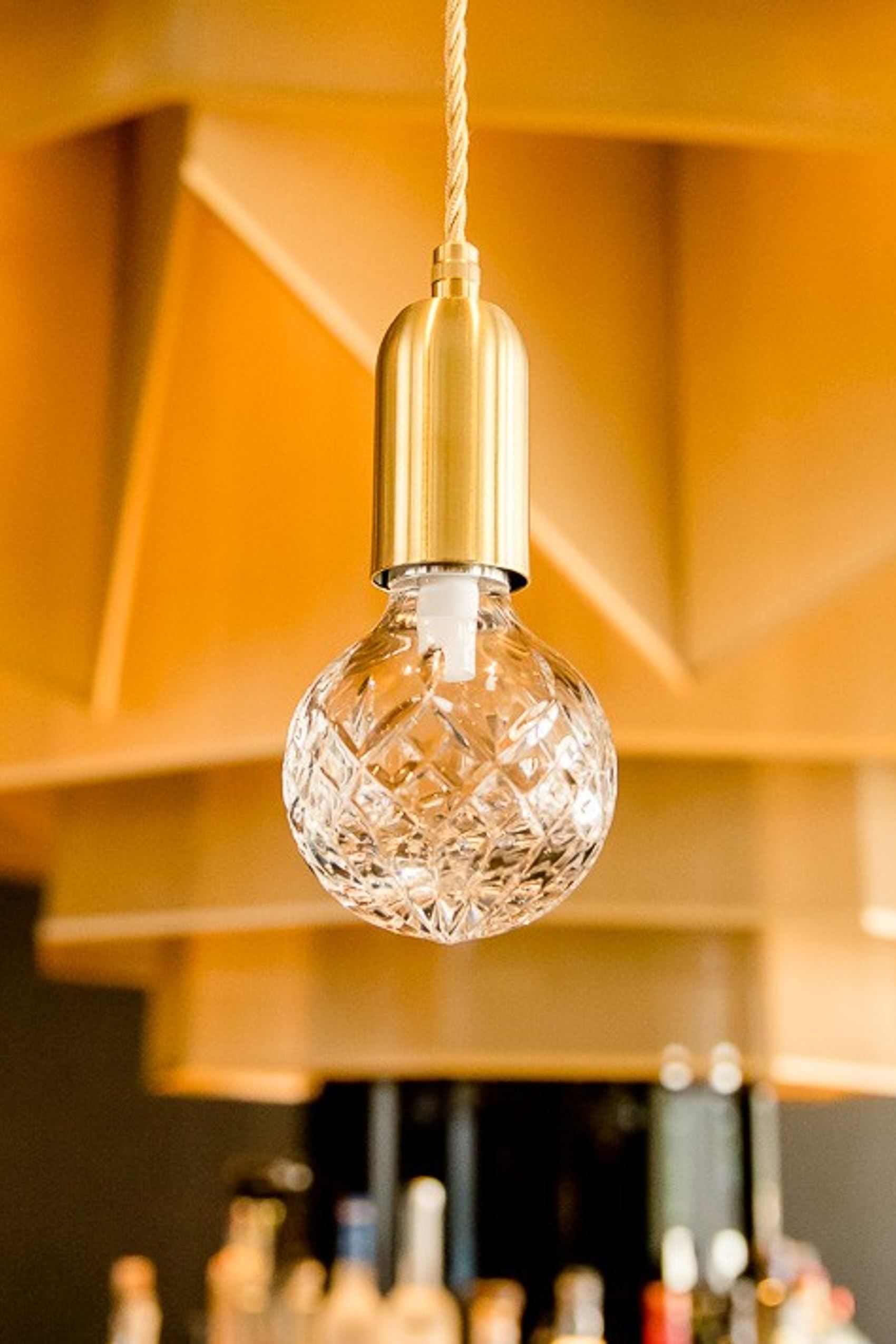 Nahaufnahme einer dekorativen Glühbirne mit goldenem Fassungsgehäuse, die in einem stilvollen, warm beleuchteten Raum hängt.