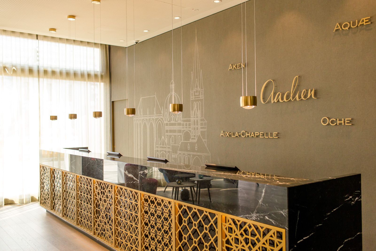 Moderner Motel One Hotellobby-Empfang mit elegantem schwarzen Marmor-Tresen und goldfarbenen dekorativen Elementen. Sanfte Beleuchtung und große Fenster.