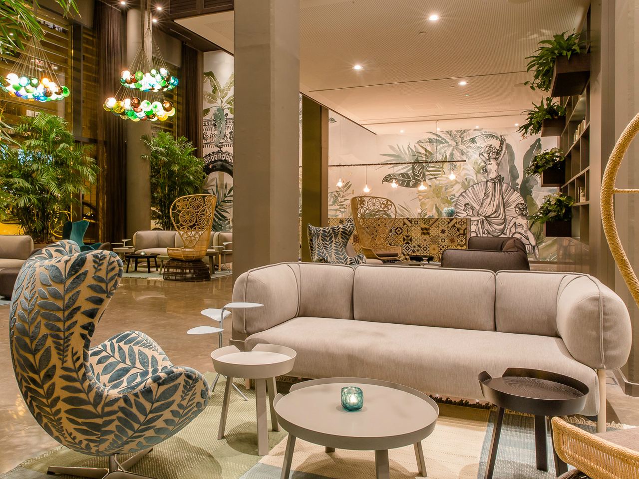 Gemütlicher, stilvoll eingerichteter Hotel-Loungebereich mit modernen Sofas, dekorativen Sesseln und grünen Pflanzen, der eine einladende Atmosphäre zum Entspannen und geselligen Beisammensein bietet.
