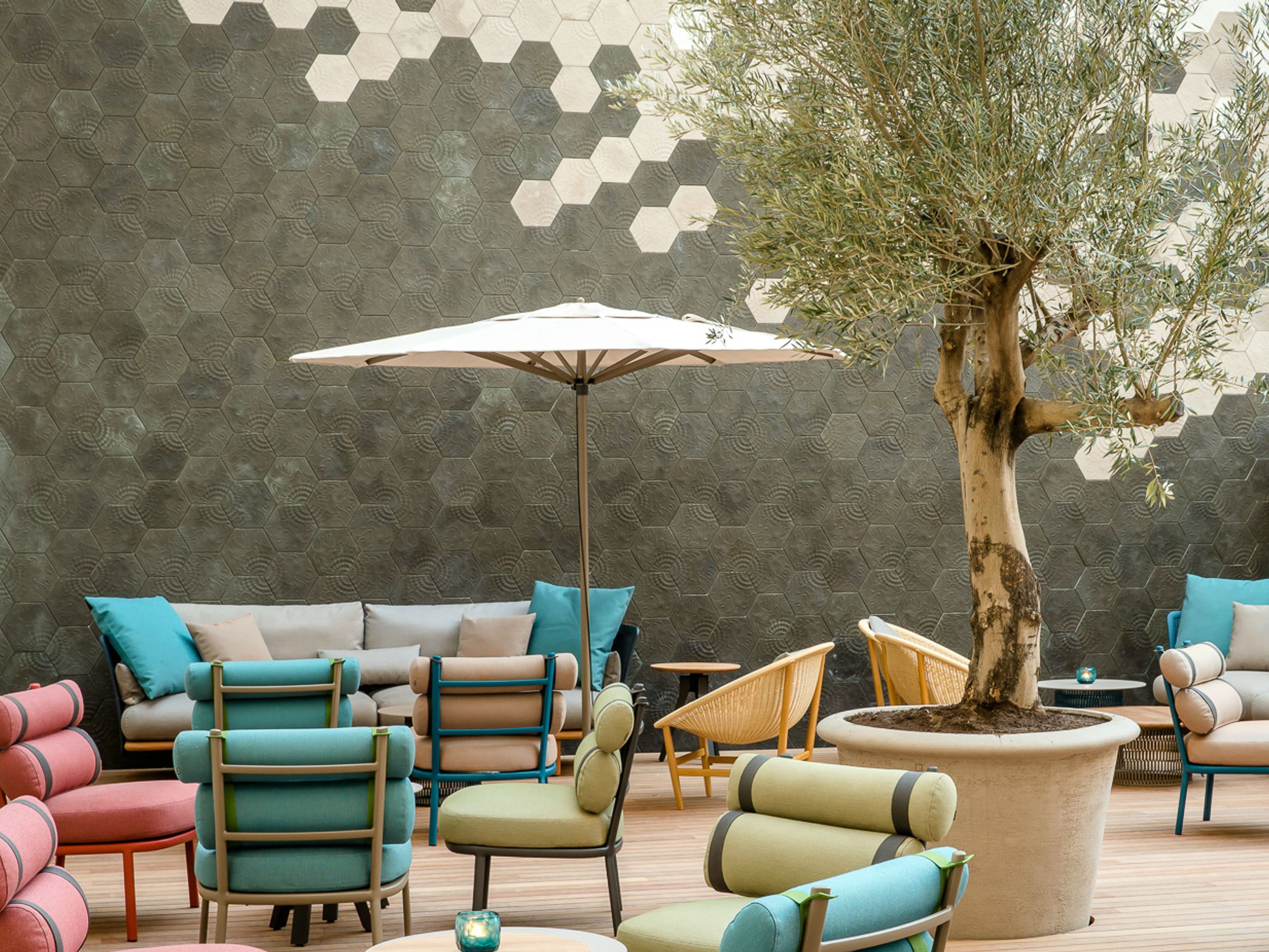 Motel One Außenlounge mit bunten Sitzmöbeln, großen Sofas und Sonnenschirm, dekorativem Baum in großem Topf