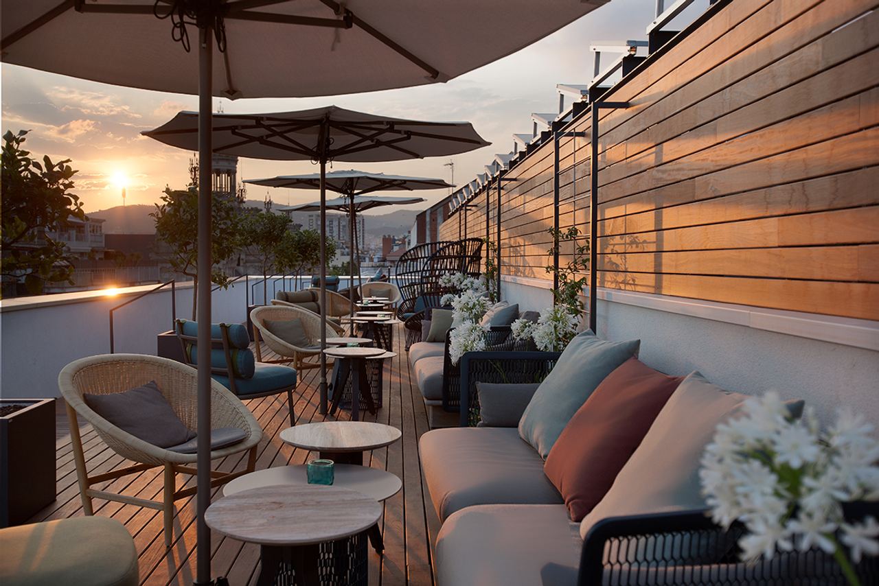 Gemütliche Dachterrasse mit modernen Sitzmöbeln, Sonnenschirmen und Pflanzen, beleuchtet vom warmen Licht des Sonnenuntergangs, ideal zum Entspannen und Genießen des Ausblicks.