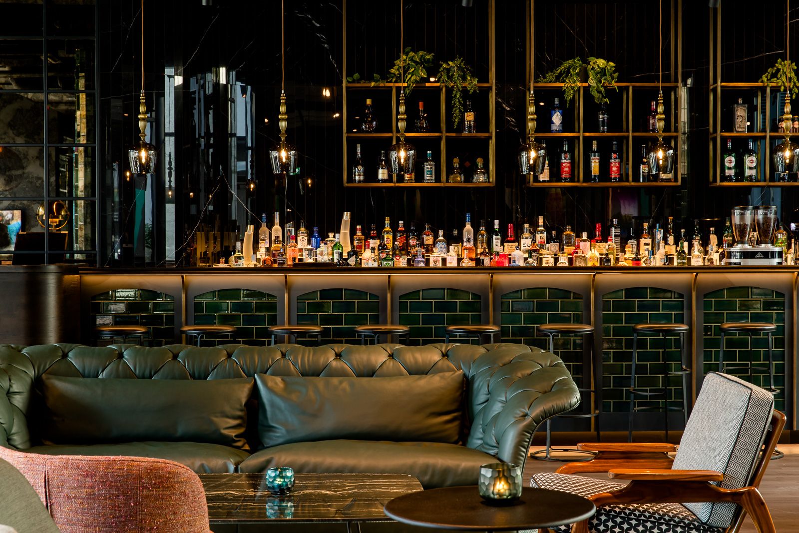 Stylishe Hotelbar mit gemütlicher Ledercouch, modernen Sesseln und beleuchteter Rückwand mit vielfältiger Spirituosenauswahl