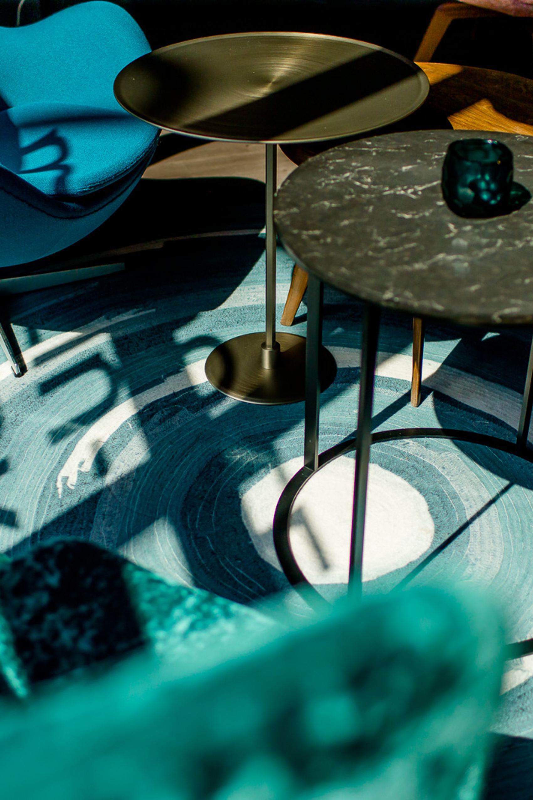 Gemütliche Sitzecke mit modernem Motel One Design, blauen und grauen Sesseln, zwei runden Tischen und einem Teppich mit wellenartigem Muster.