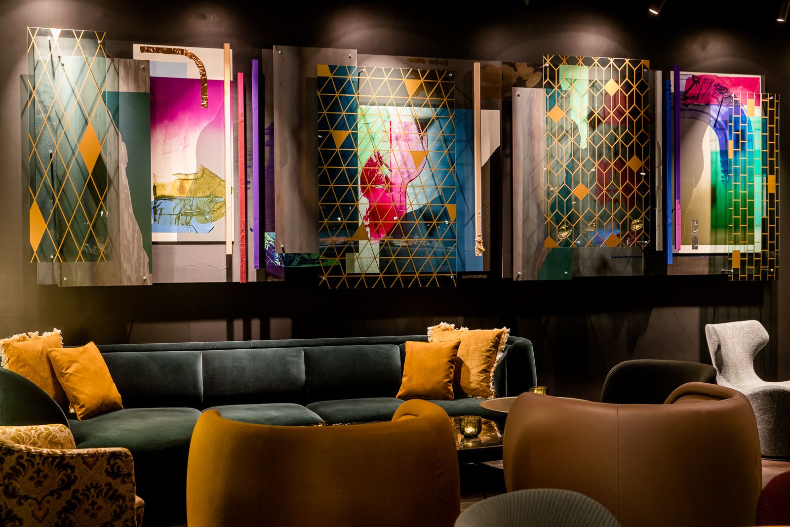 Moderner Lounge-Bereich mit dunkelgrünem Sofa, bunten Kissen und stilvollen Sitzmöbeln. An der Wand befindet sich eine große, abstrakte Kunstinstallation mit leuchtenden Farben und geometrischen Mustern