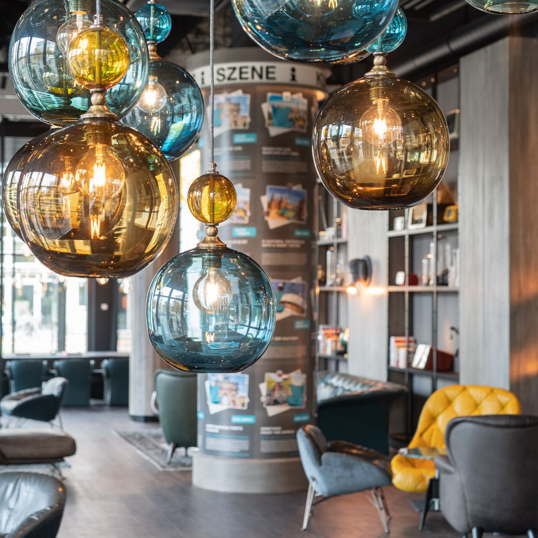 Bunte, kugelförmige Pendelleuchten in warmem Licht dekorieren eine stilvolle Hotellounge mit modernen Sesseln und gemütlicher Atmosphäre.
