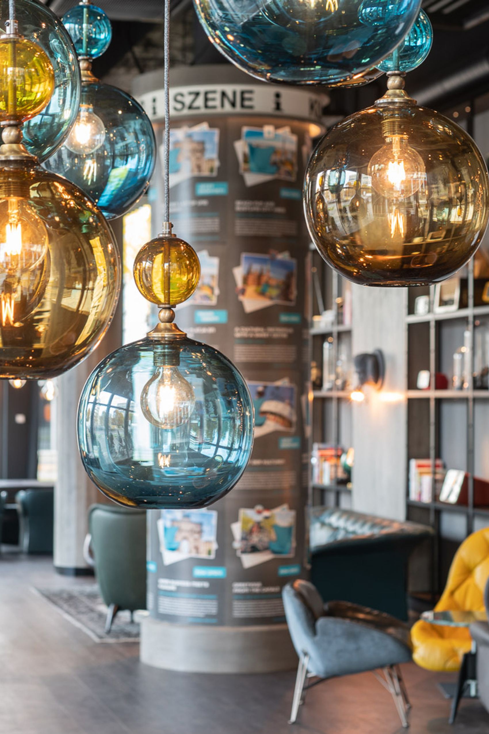 Bunte, kugelförmige Pendelleuchten in warmem Licht dekorieren eine stilvolle Hotellounge mit modernen Sesseln und gemütlicher Atmosphäre.