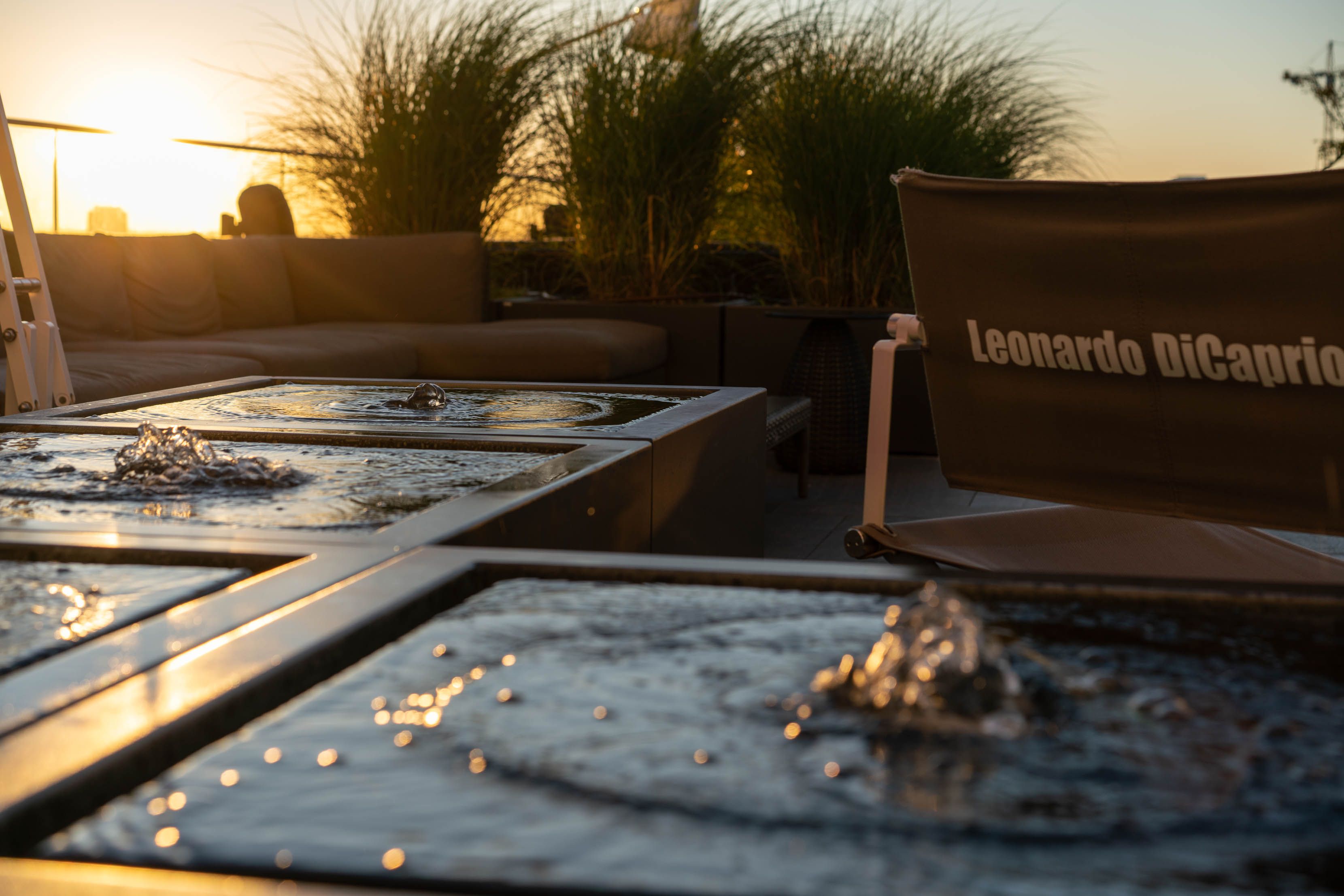 Loungebereich mit gemütlichen Sitzmöbeln und Wasserfontänen bei Sonnenuntergang