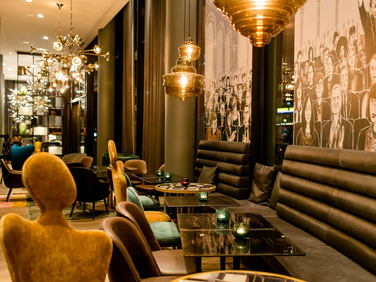 Motel One Hotelbar mit stilvoller Beleuchtung, bequemen Sitzbänken und Sesseln. Wände geschmückt mit großen Schwarz-Weiß-Porträts