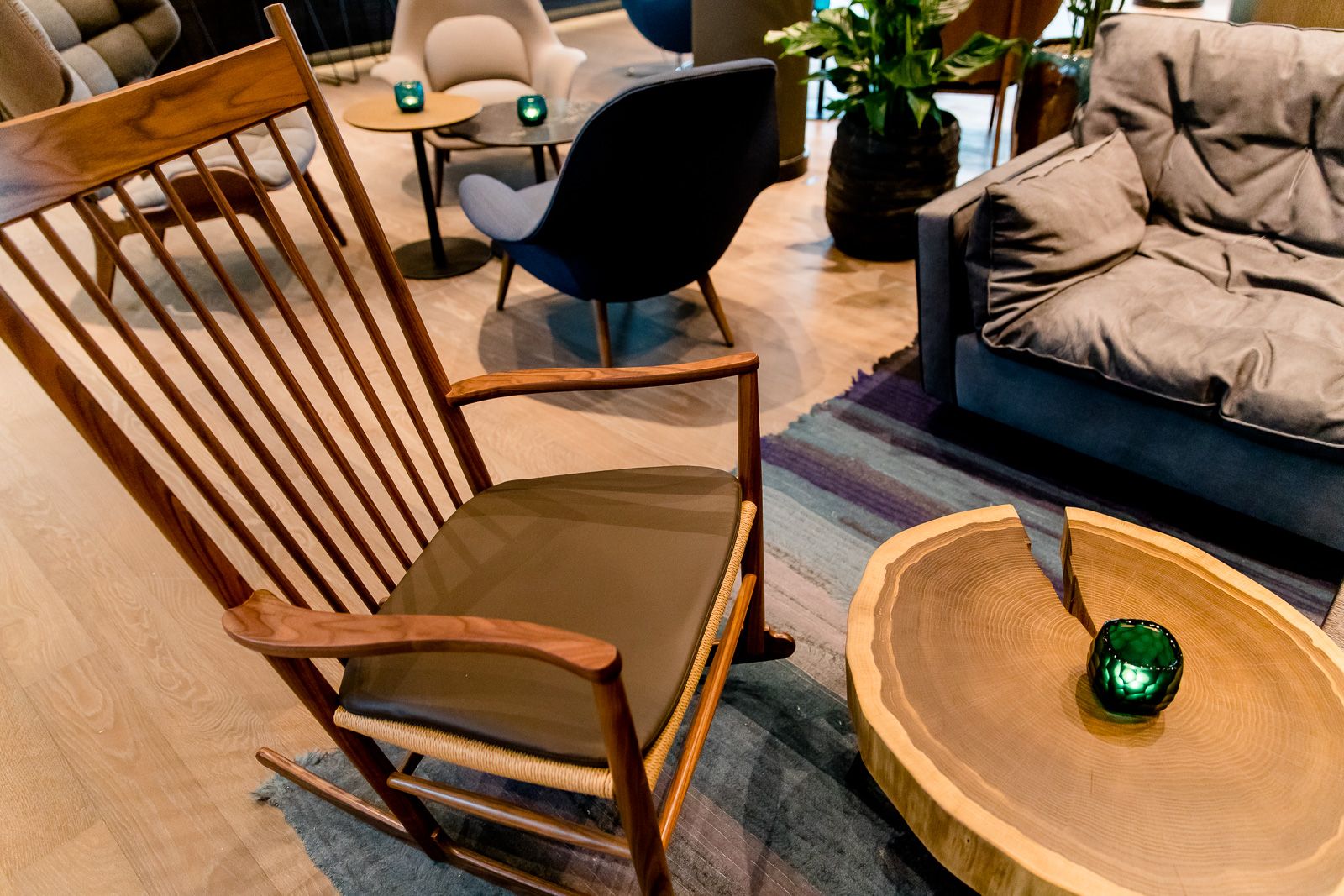 Gemütliche Sitzecke mit einem Holzschaukelstuhl, einem runden Holztisch und mehreren Polstersesseln, warme Beleuchtung und dekorative grüne Kerzen 