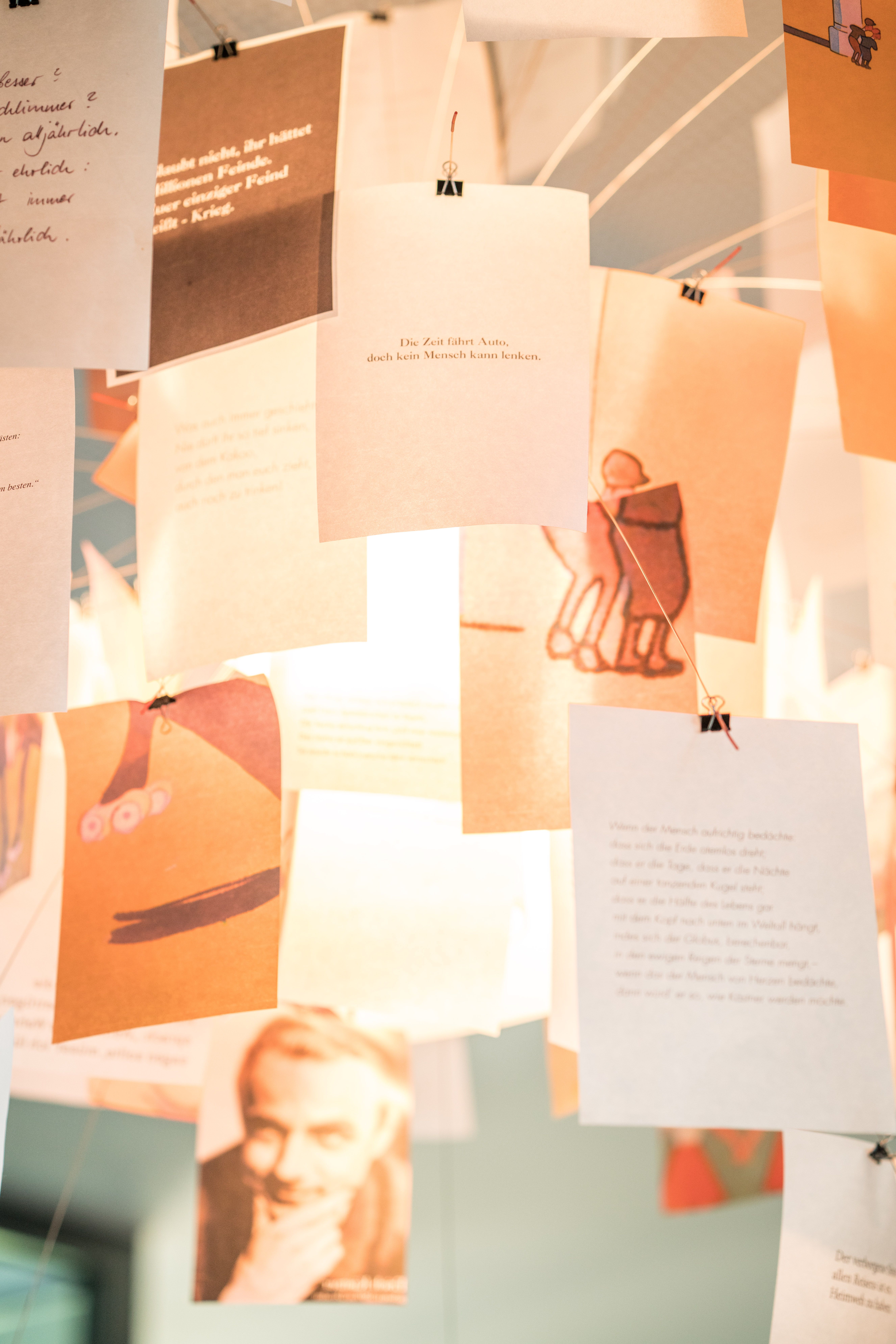 Mehrere Papierblätter mit Texten und Illustrationen hängen dekorativ von der Decke im Motel One und erzeugen eine kreative, inspirierende Atmosphäre.