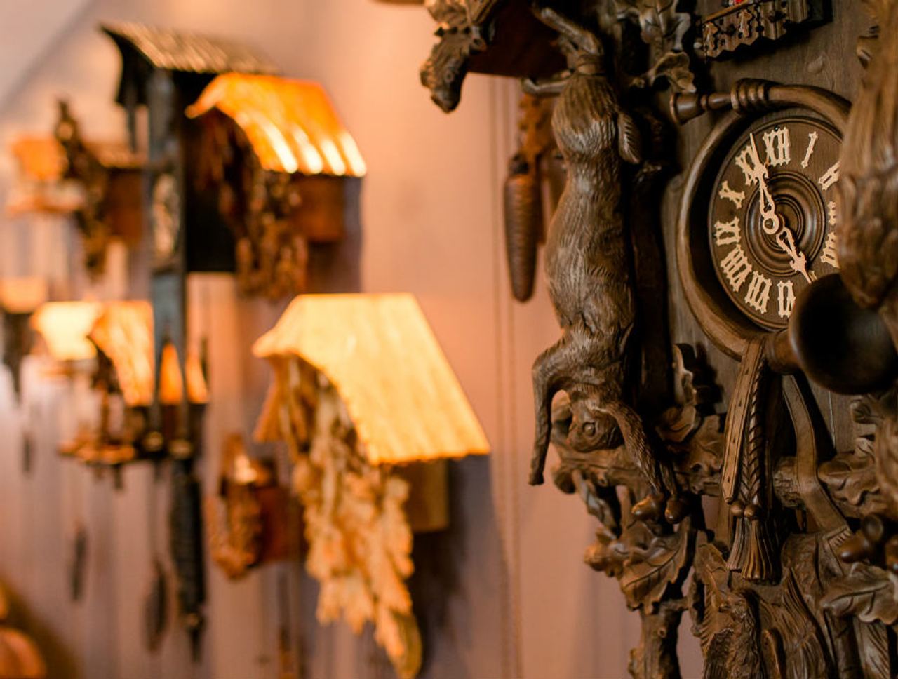 Detailreiche, traditionell geschnitzte Kuckucksuhren an einer Wand, warm beleuchtet