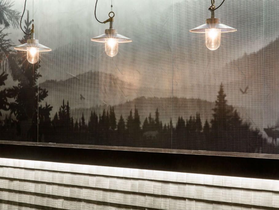 Drei industriell gestaltete Hängelampen erleuchten eine gemütliche Innenwand mit Naturmotiv, das Berglandschaft und Nadelbäume zeigt