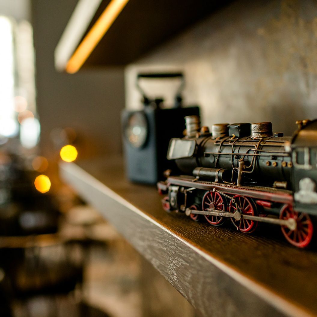 Detailaufnahme einer nostalgischen Modell-Lok aus Metall auf einem Holzregal, umgeben von warmem Licht.