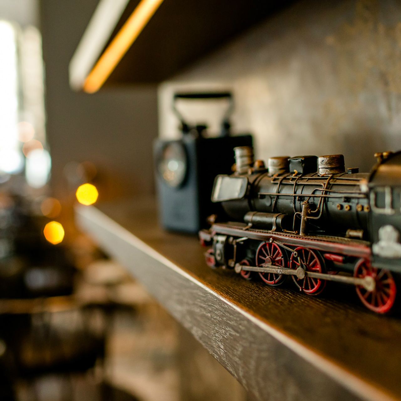 Detailaufnahme einer nostalgischen Modell-Lok aus Metall auf einem Holzregal, umgeben von warmem Licht.