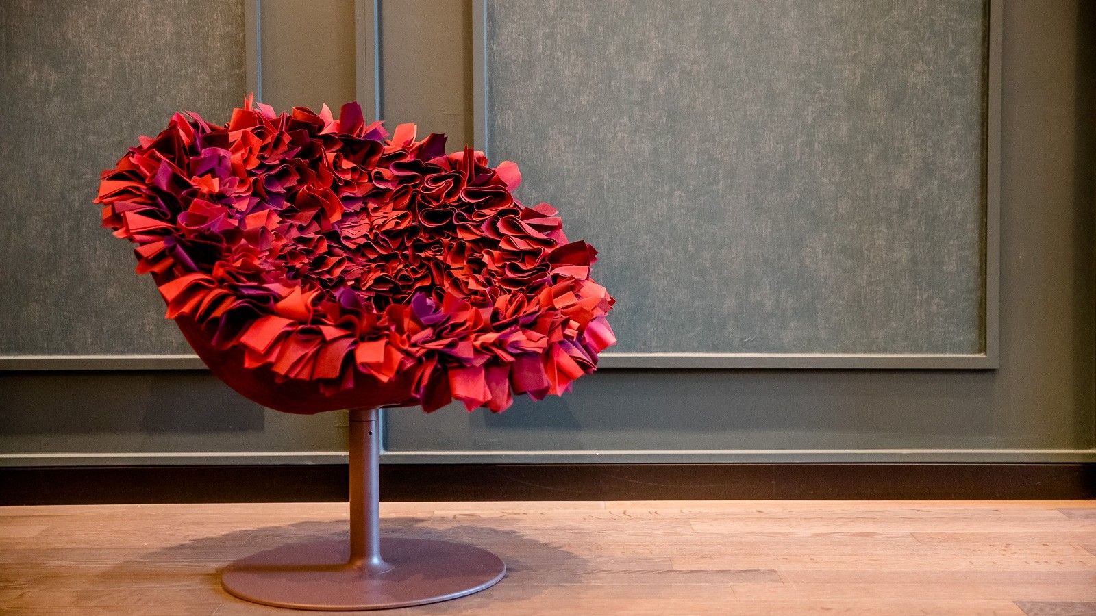 Moderner roter Sessel mit auffälligem, wellenförmigem Polsterdesign in einem stilvollen, ruhigen Raum mit Holzboden und grüner Wand, der einen außergewöhnlichen Sitzkomfort und kreatives Ambiente vermittelt.