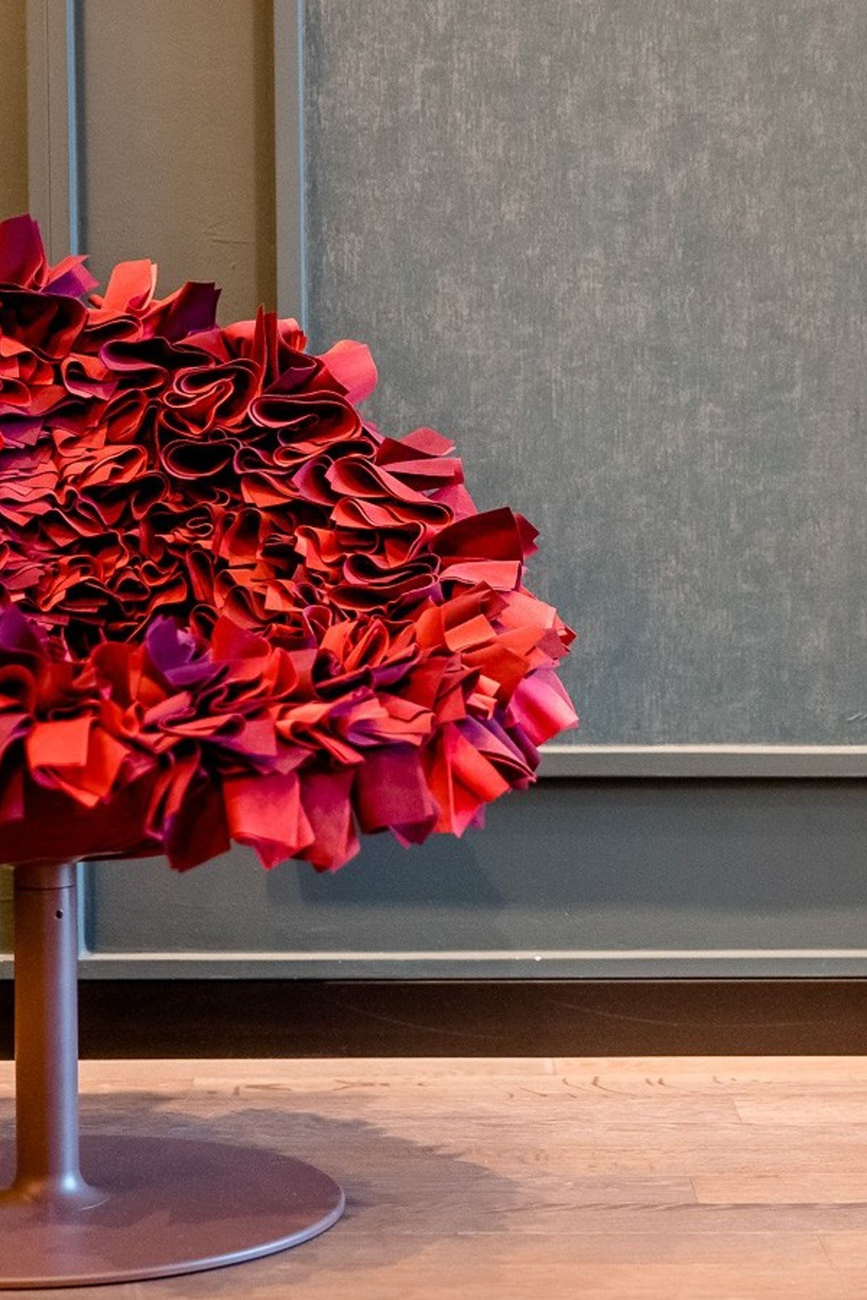 Motel One roter Design Sessel mit auffälligem, wellenförmigem Polsterdesign in einem stilvollen, ruhigen Raum mit Holzboden und grüner Wand, der einen außergewöhnlichen Sitzkomfort und kreatives Ambiente vermittelt.