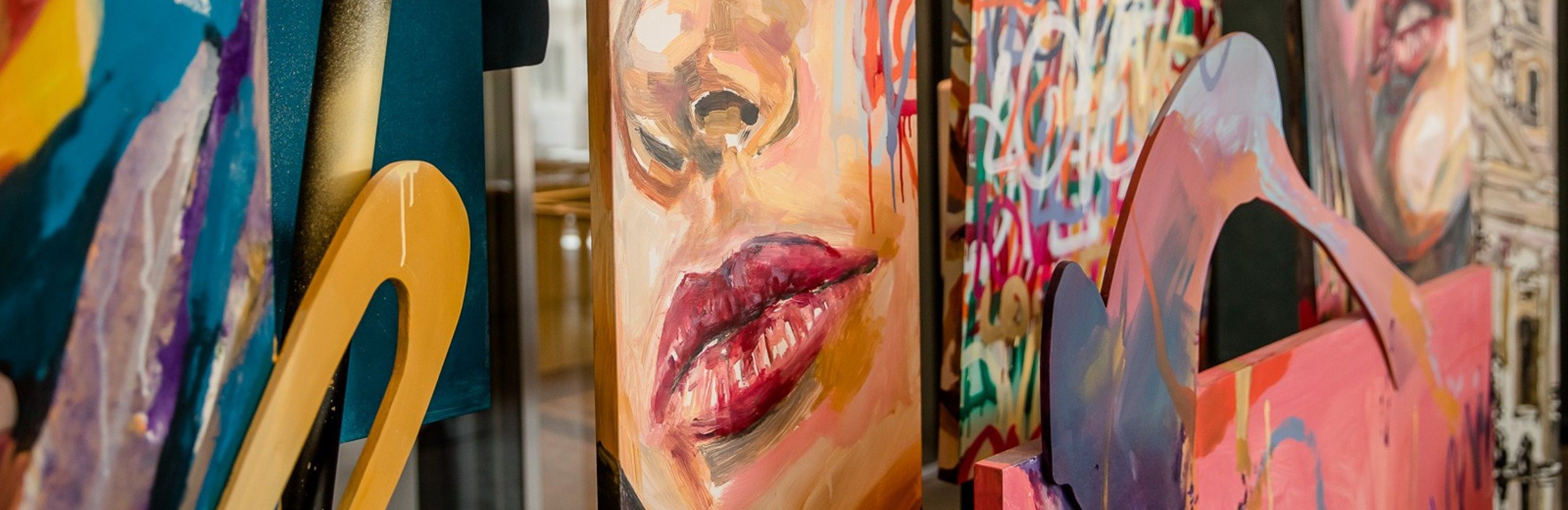 Nahaufnahme bunter, moderner Gemälde mit abstrakten und realistischen Gesichtsdarstellungen, die kreative Kunst in lebendigen Farben zeigen.