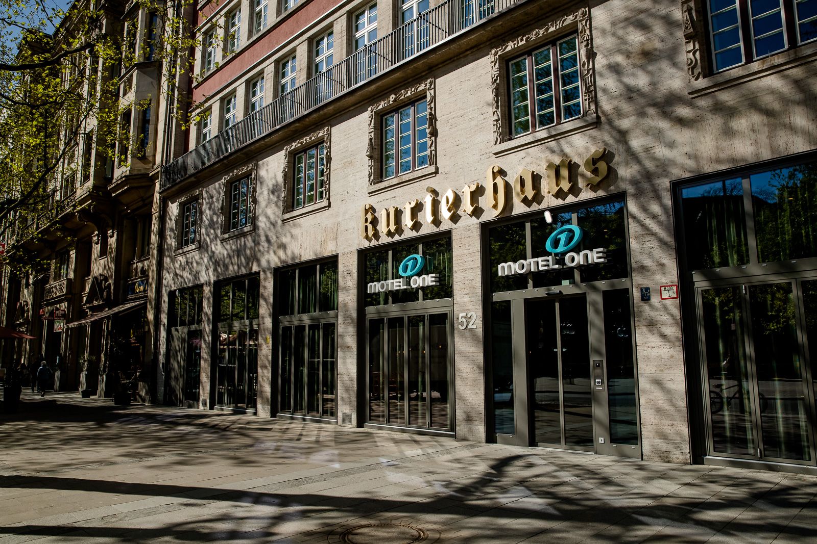 Fassade des Motel One Hotels in einem historischen Gebäude mit großen Fenstern und dem Schriftzug „Kurierhaus“ bei Tageslicht.