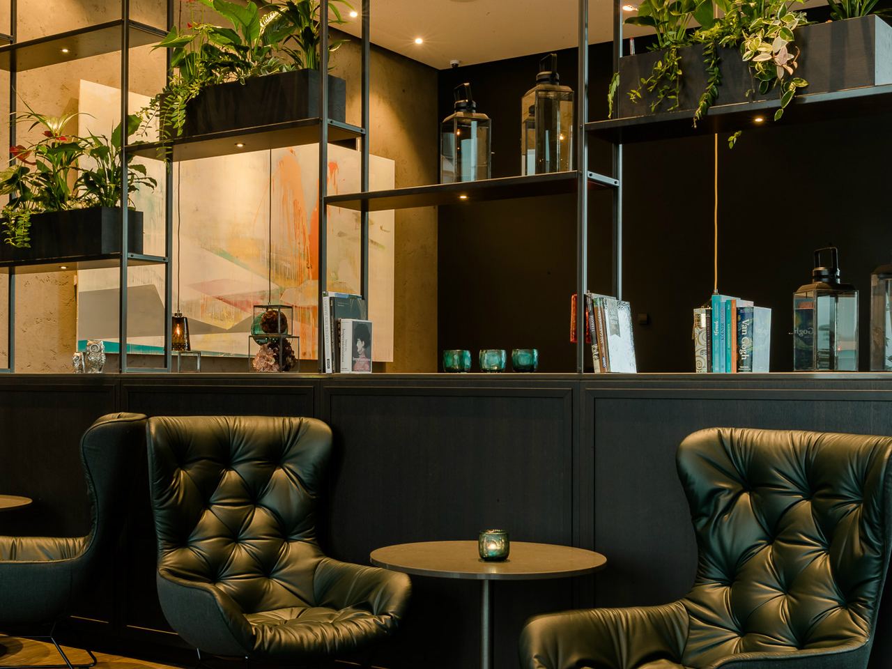 Gemütliche Sitzecke mit zwei dunkelgrünen, gepolsterten Sesseln und kleinem runden Tisch, umgeben von moderner Raumtrennung mit Pflanzen und stimmungsvoller Beleuchtung