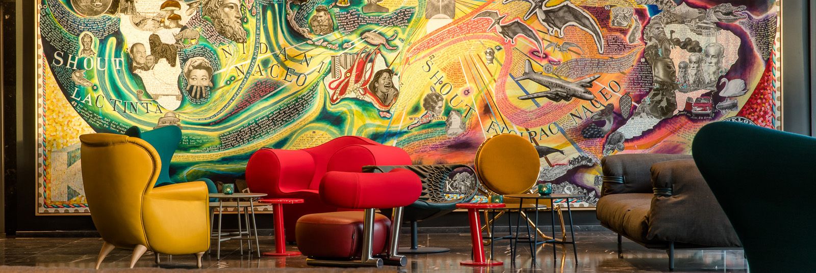 Moderner Lobbybereich mit bunten Designer-Sesseln und Sofas vor einer großflächigen, farbenfrohen Wandmalerei, die historische und künstlerische Motive zeigt. 