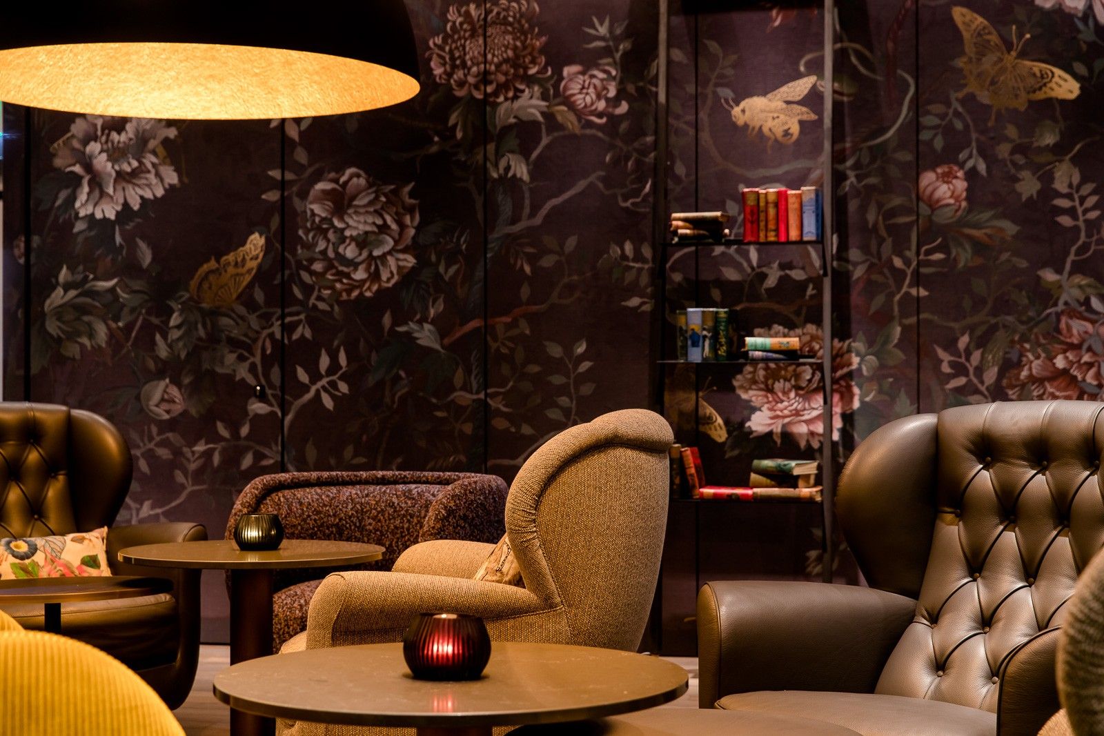 Gemütliche Motel One Lounge mit bequemen Sesseln, dunkler floraler Tapete und warmem Licht