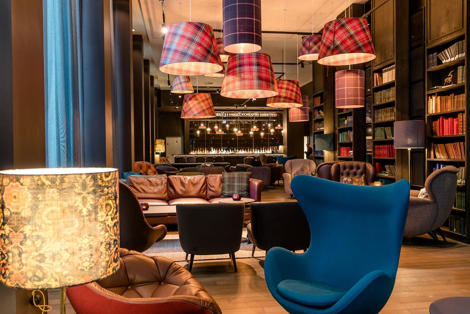 Gemütlicher Hotel-Loungebereich mit bequemen Sesseln, Ledersofas und warmem Licht. Große Bücherregale und dekorative Lampenschirme.