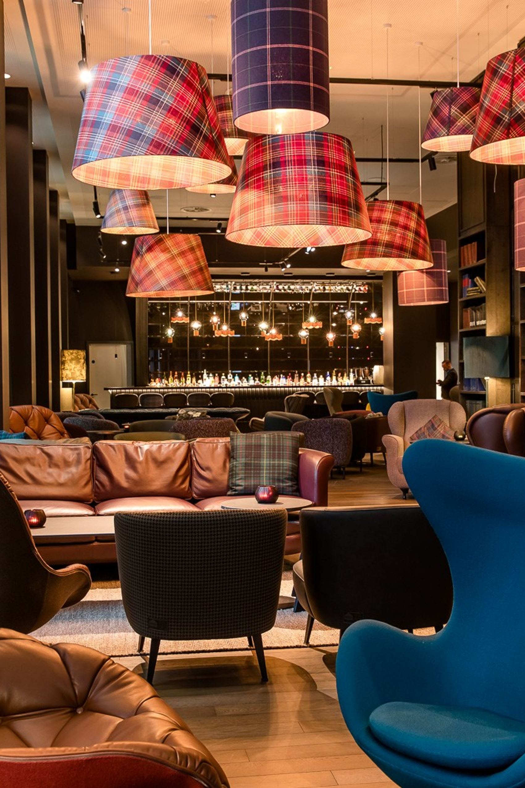 Gemütlicher Hotel-Loungebereich mit bequemen Sesseln, Ledersofas und warmem Licht. Große Bücherregale und dekorative Lampenschirme.