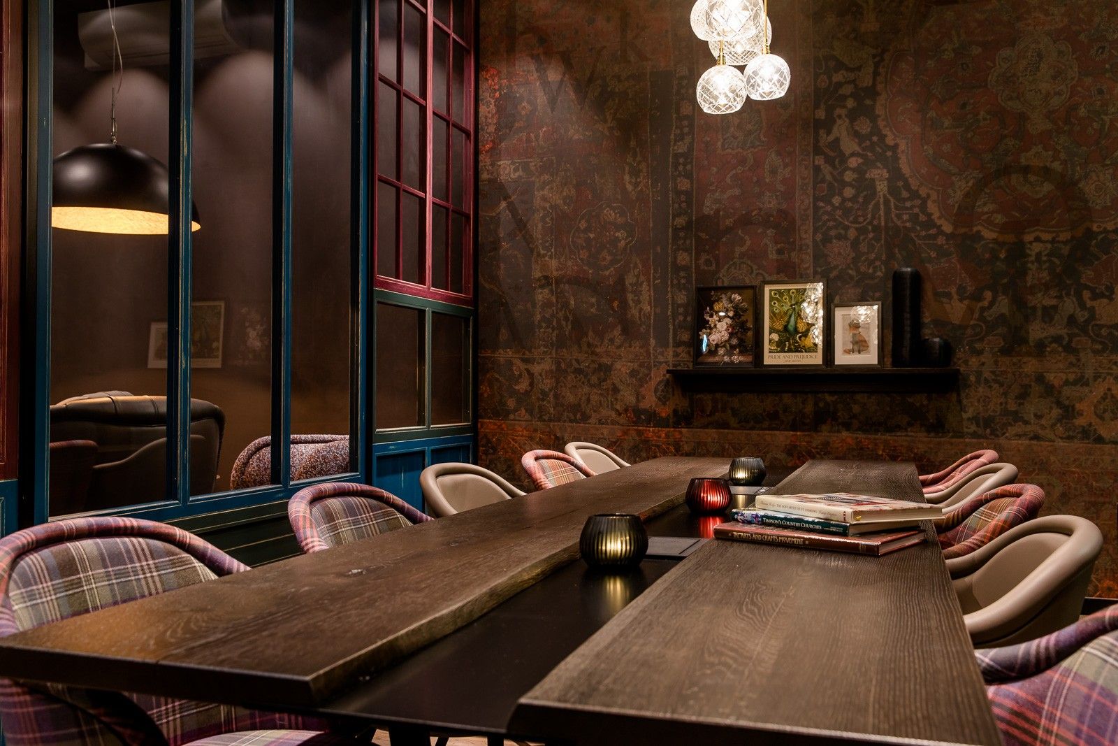 Gemütlicher, eleganter Besprechungsraum mit langem Holztisch, gepolsterten Stühlen in Karomuster, warmen Lichtakzenten und dekorativen Bildern an der Wand für stilvolle Meetings oder entspannte Gespräche.