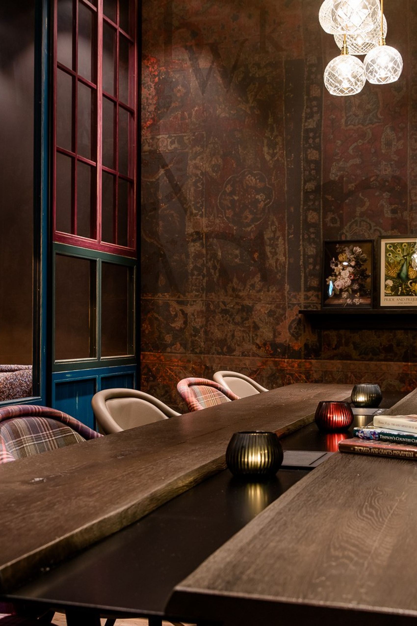 Gemütlicher, eleganter Besprechungsraum mit langem Holztisch, gepolsterten Stühlen in Karomuster, warmen Lichtakzenten und dekorativen Bildern an der Wand für stilvolle Meetings oder entspannte Gespräche.