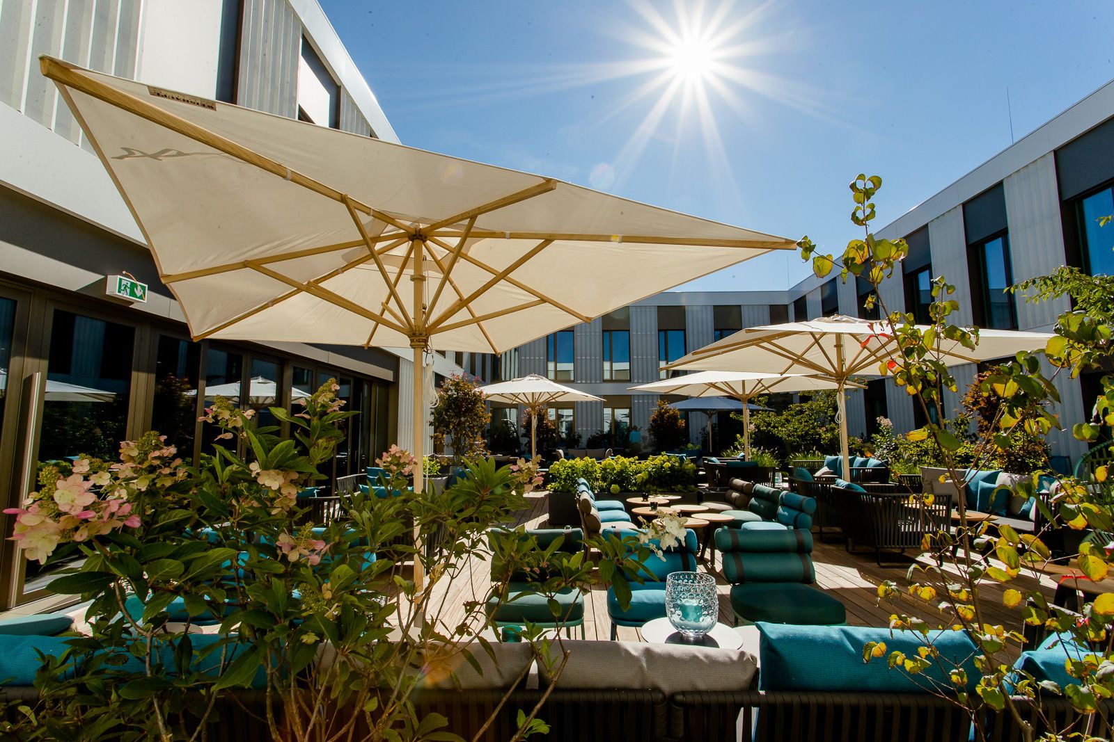 Sonniger Motel One Hotel-Innenhof mit gemütlichen Sitzbereichen, großen Sonnenschirmen und grünen Pflanzen.