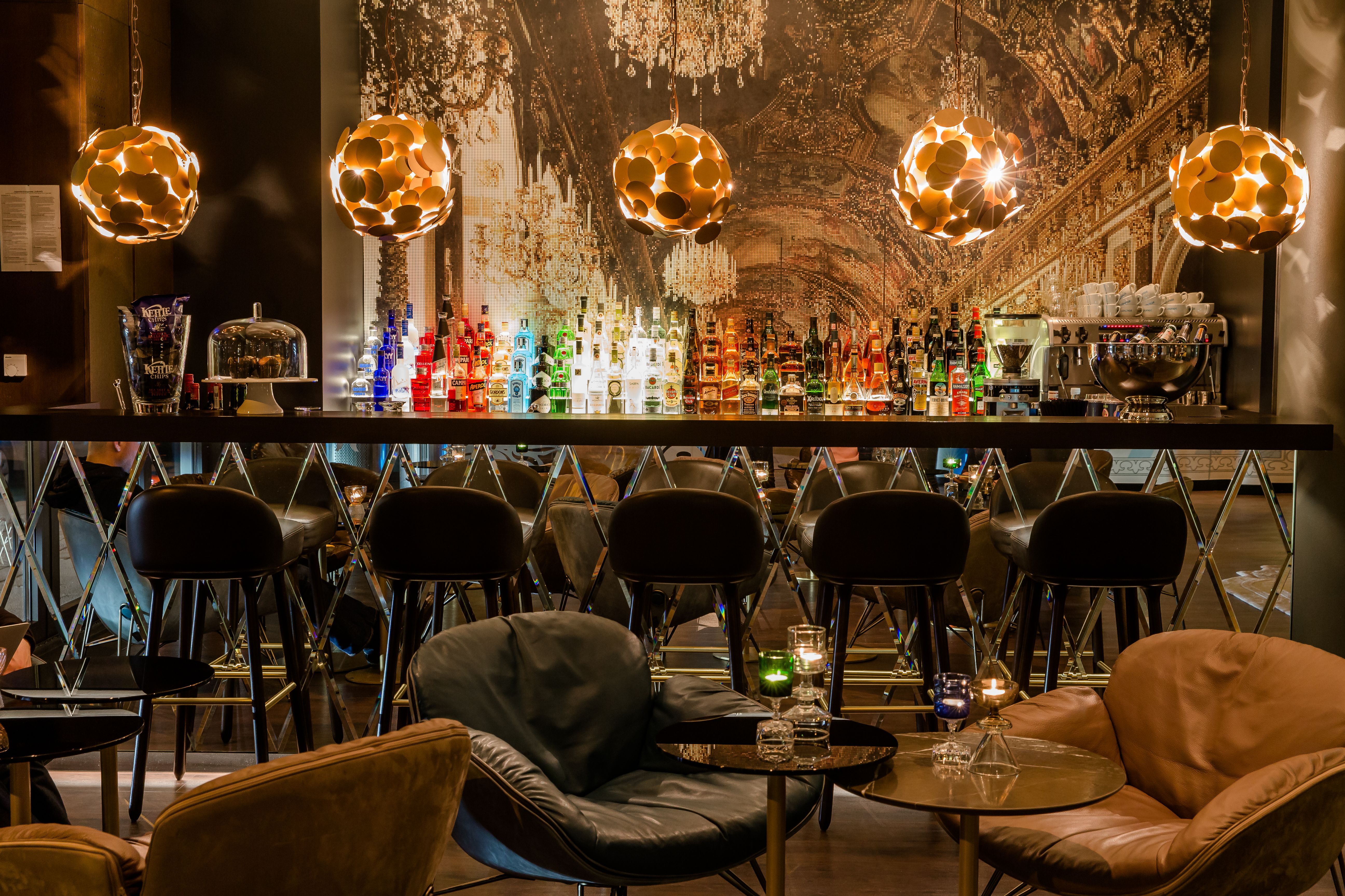 Motel One Hotelbar mit stilvoller Beleuchtung, bequemen Sesseln und einer großen Auswahl an bunten Spirituosen.