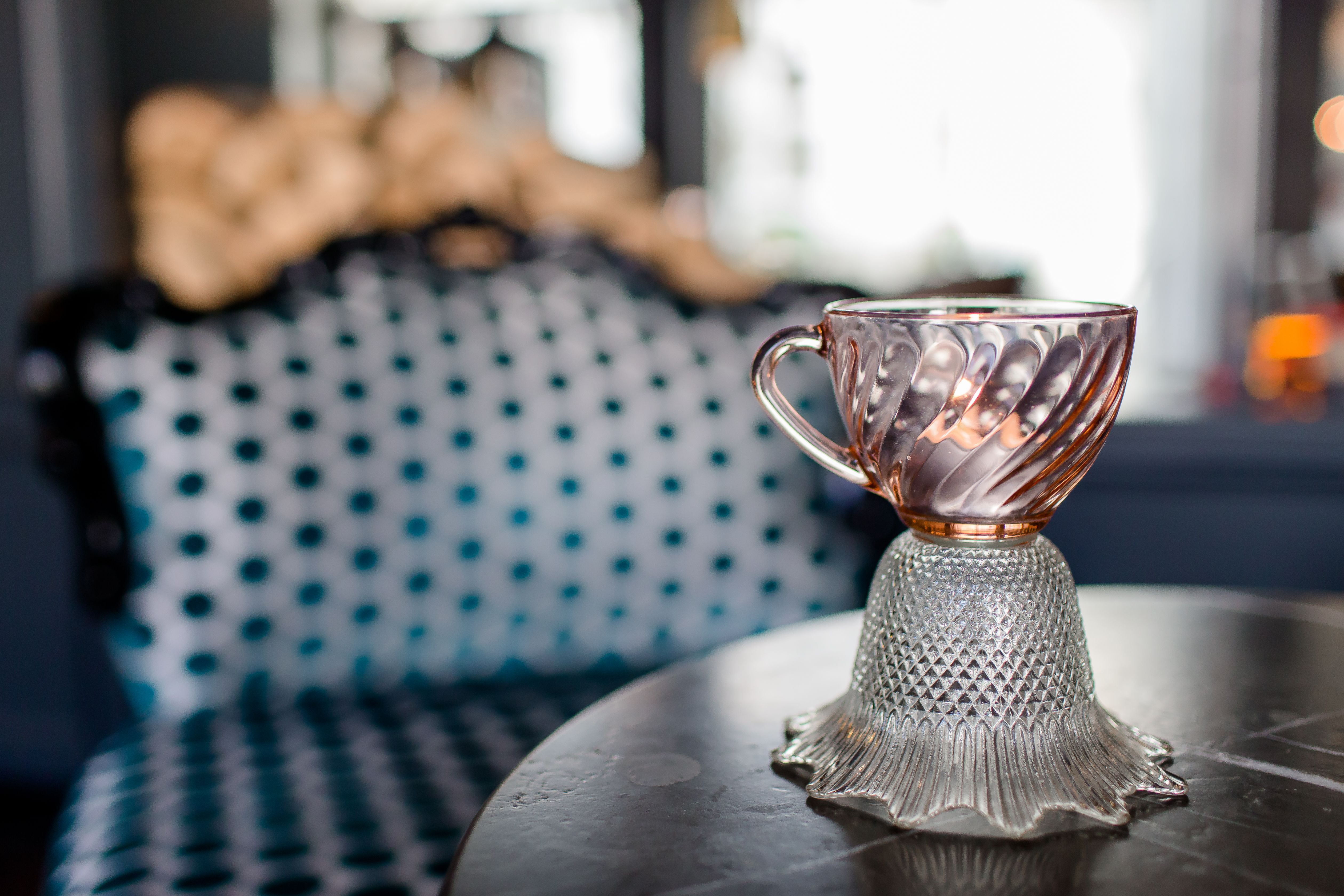 Elegante, kunstvoll gestaltete Glas-Tasse, die auf einem Tisch steht, vor unscharfem Hintergrund mit stilvoller Polsterung.