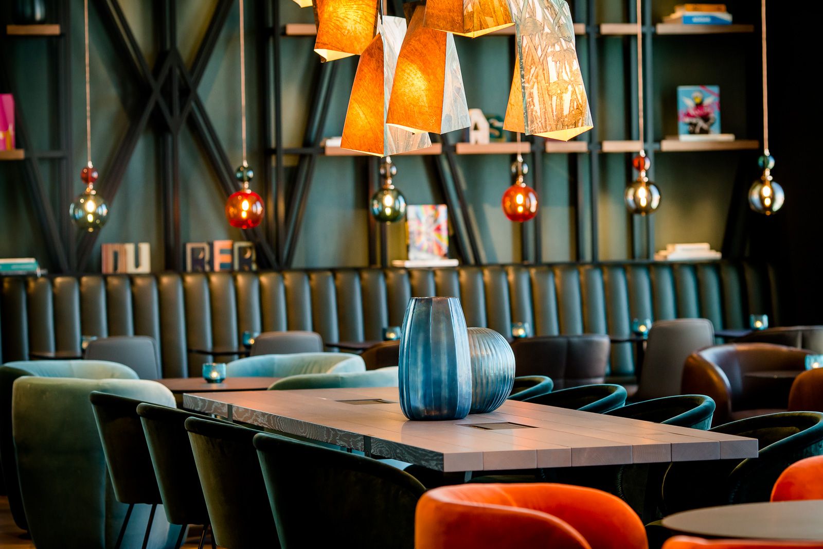 Hotelbarbereich mit modernem Holztisch, bequemen Sesseln in dunklen und orangefarbenen Tönen, dekorativen Lampen und stilvollen Vasen als Tischdekoration