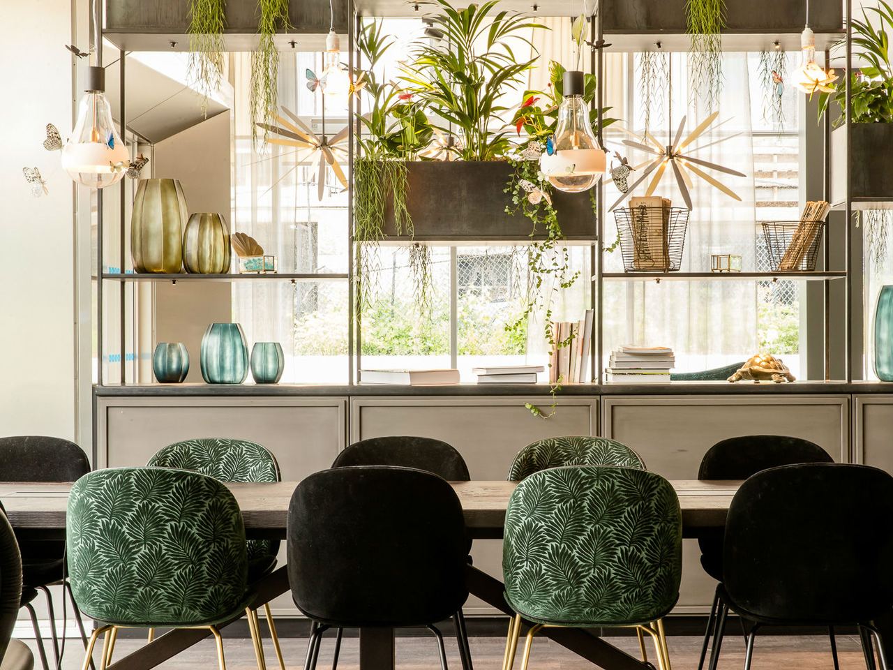 Motel One Essbereich mit stilvollen, gepolsterten Stühlen, viel natürlichem Licht und grünen Pflanzen